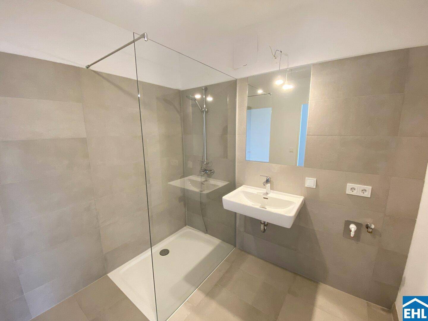 Modernes Badezimmer mit großformatigen grauen Fliesen, ebenerdiger Dusche und Wandwaschbecken.