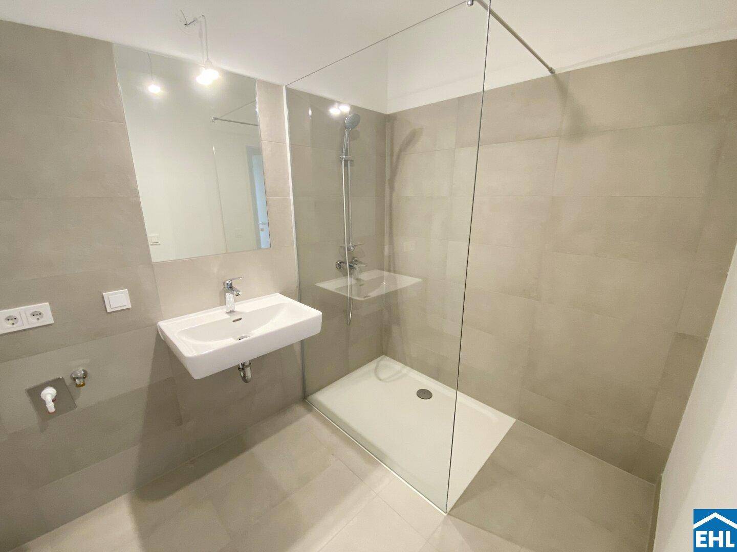 Modernes Badezimmer mit grauen Fliesen, ebenerdiger Dusche und elegantem Waschbecken.
