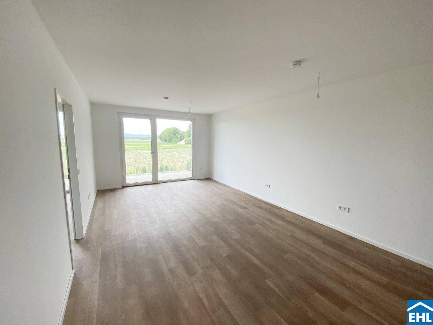 Geräumiges Wohnzimmer mit Laminatboden und großem Fenster mit Blick auf die Landschaft.