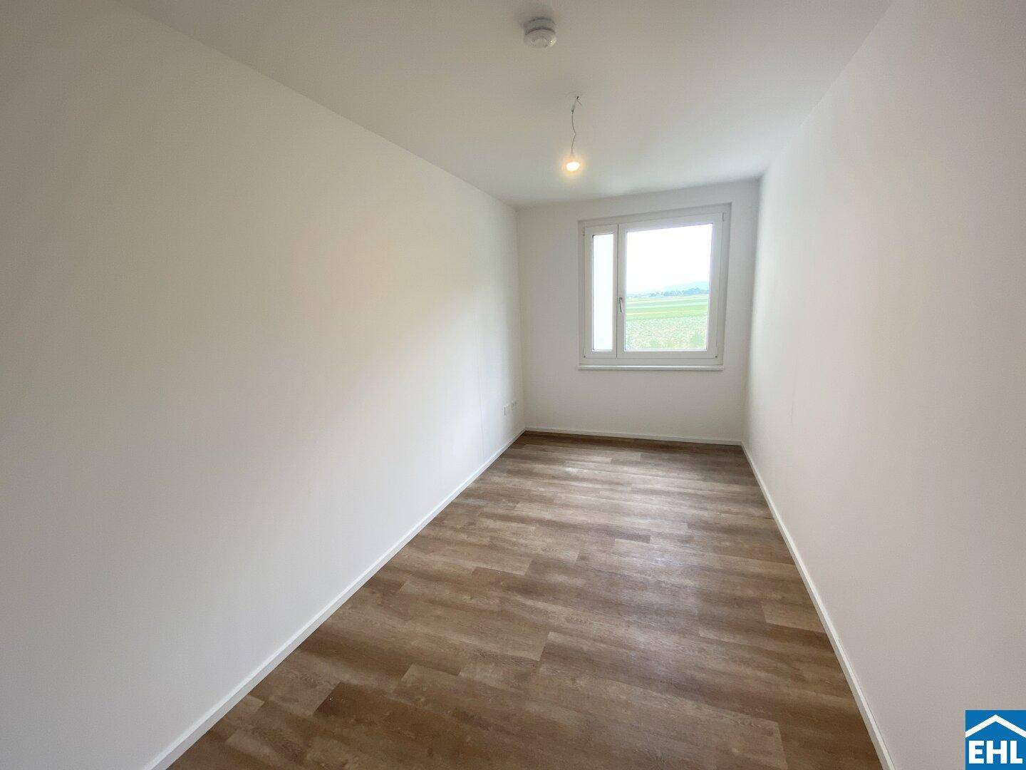 Leeres Schlafzimmer mit hellem Laminatboden und weitem Blick auf die umliegende Landschaft.