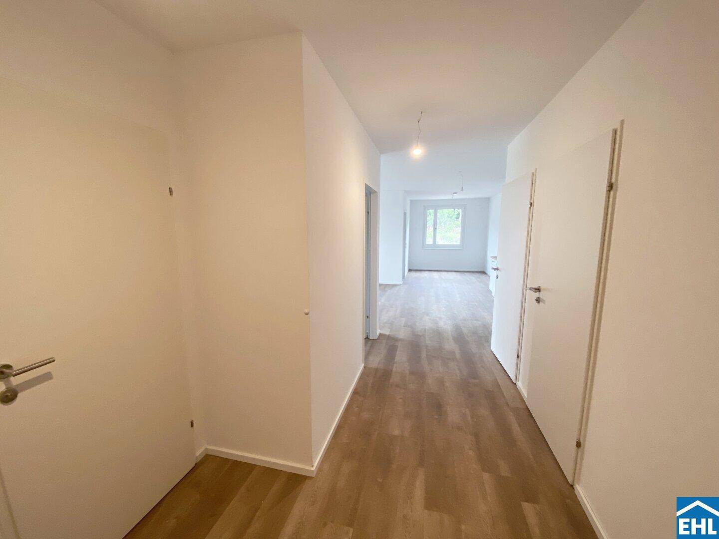 Heller Flur mit modernem Laminatboden, weißen Wänden und Zugang zu weiteren Räumen.