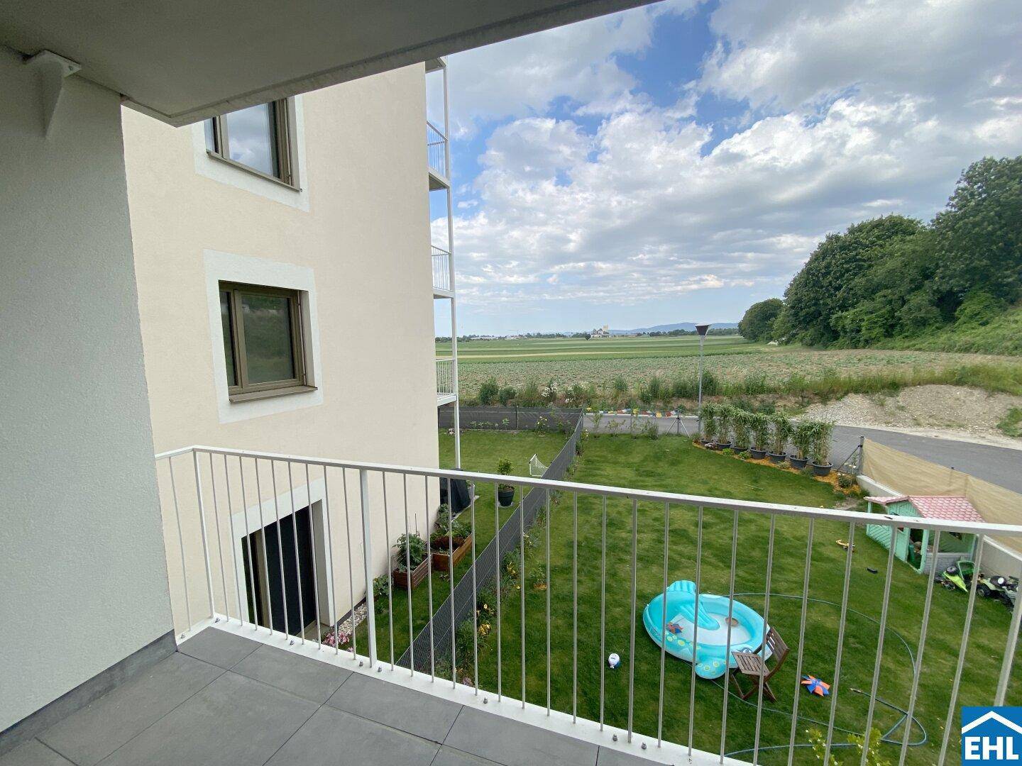 Balkon mit Blick auf einen kleinen Garten und weite grüne Felder in der Ferne.