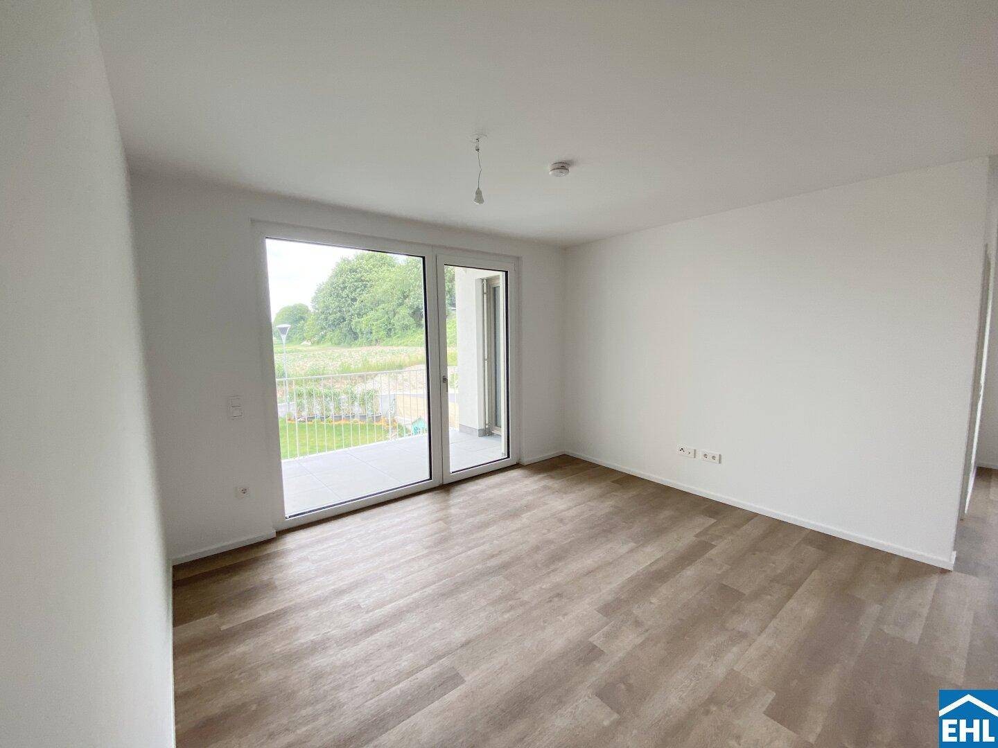 Lichtdurchflutetes Wohnzimmer mit Laminatboden und weitem Blick ins Grüne vom Balkon.