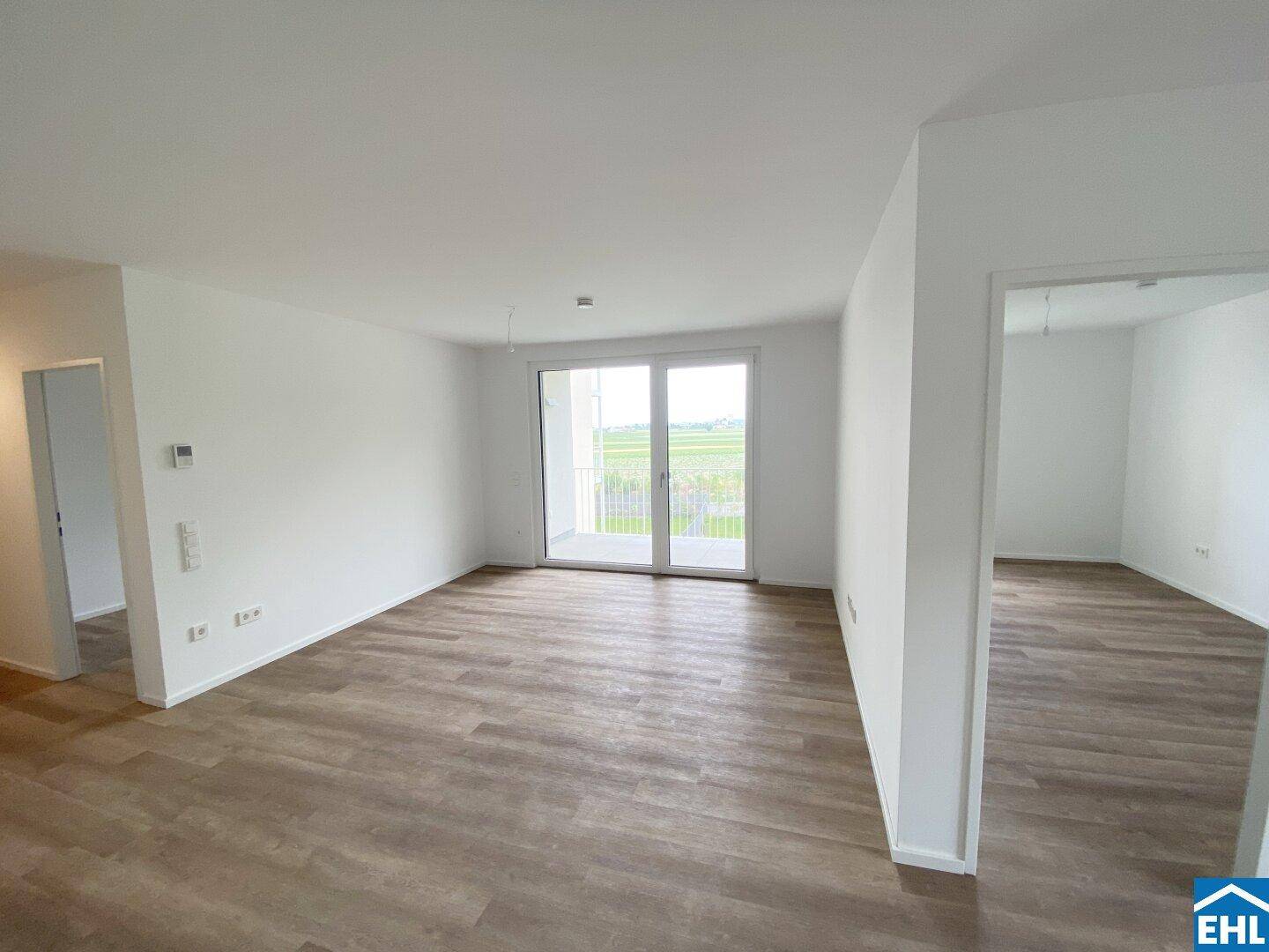 Helles Wohnzimmer mit Laminatboden, großen Fenstern und direktem Zugang zum Balkon.