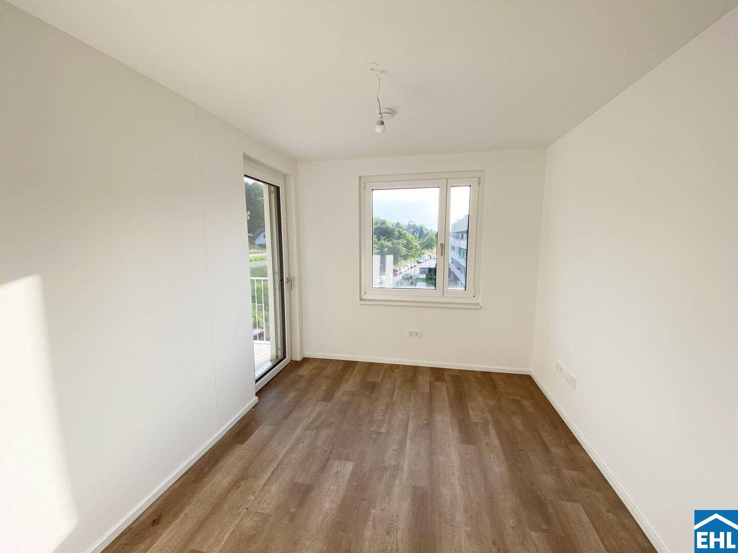Helles Zimmer mit Laminatboden, weißen Wänden und Zugang zu einem kleinen Balkon.