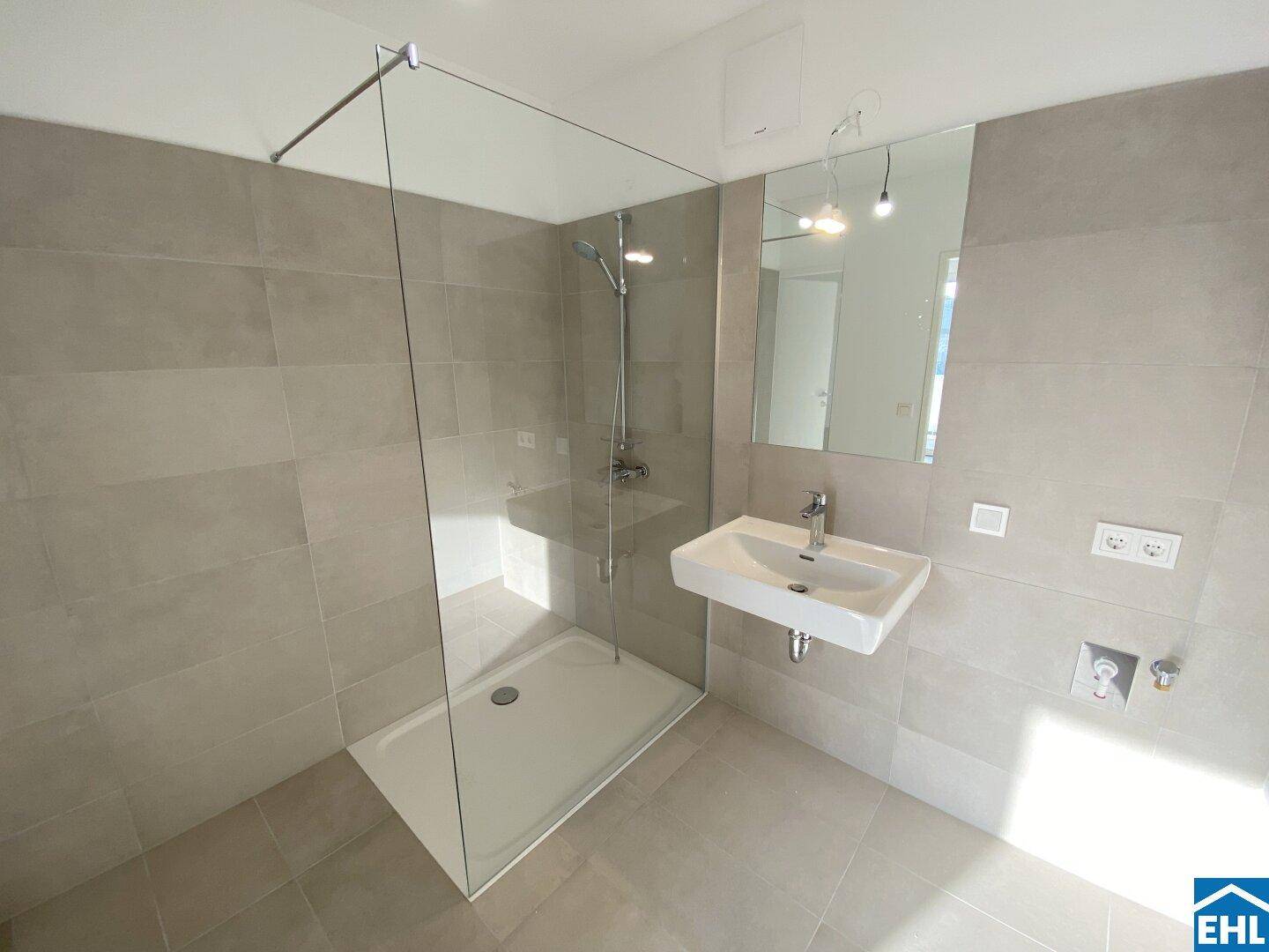 Modernes Badezimmer mit hellgrauen Fliesen, einer begehbaren Dusche und einem Wandwaschbecken.