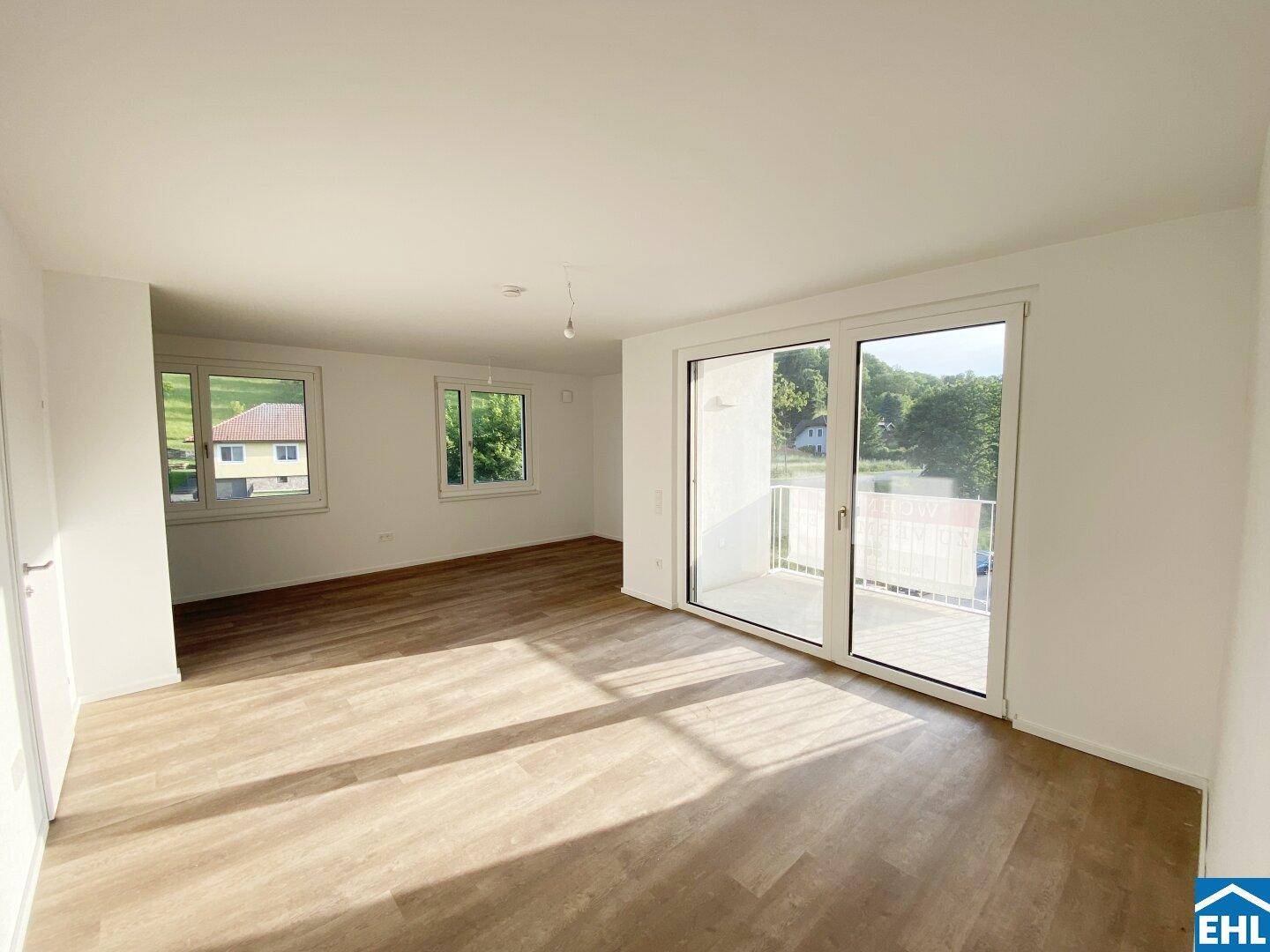 Geräumiges Wohnzimmer mit Laminatboden, großen Fenstern und Zugang zu einem sonnigen Balkon.