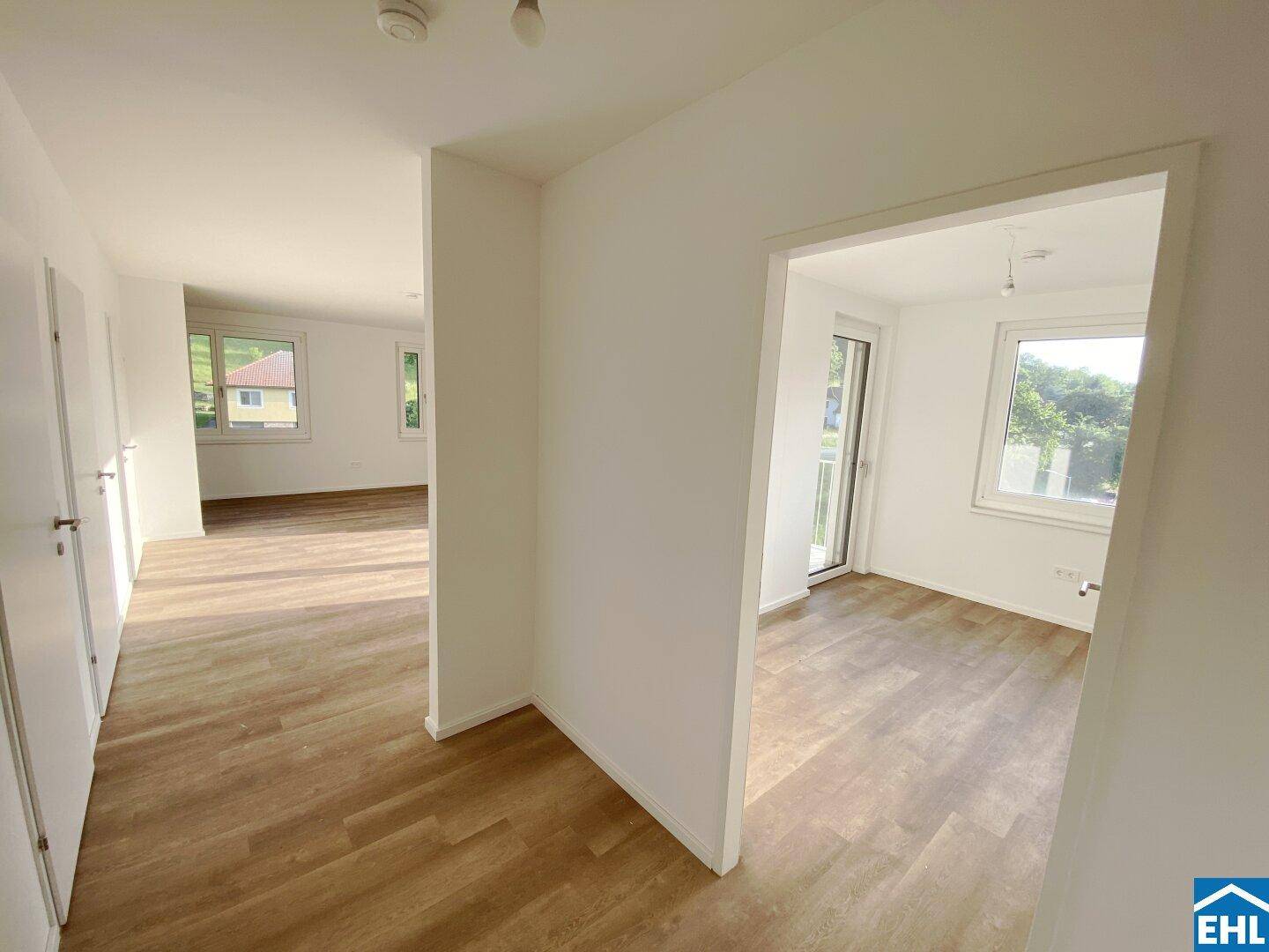 Heller Flur mit Holzboden, der zu weiteren leeren Zimmern mit großen Fenstern führt.