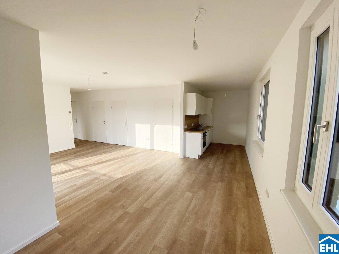Offener Wohnbereich mit integrierter Küchenzeile, Holzboden und viel natürlichem Licht.