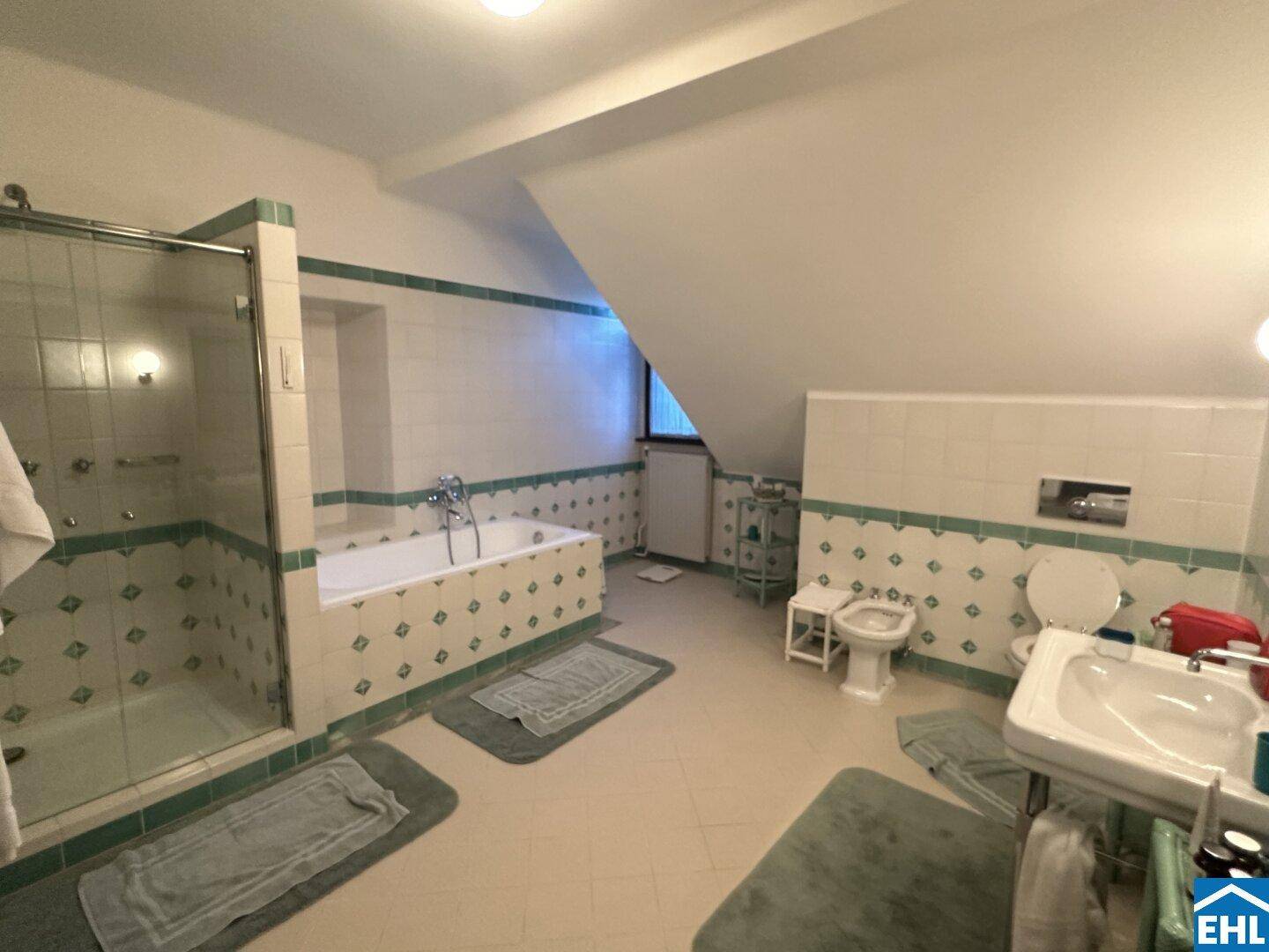 Geräumiges Badezimmer mit grünen und weißen Fliesen, Badewanne und separater Dusche unter Dachschräge.