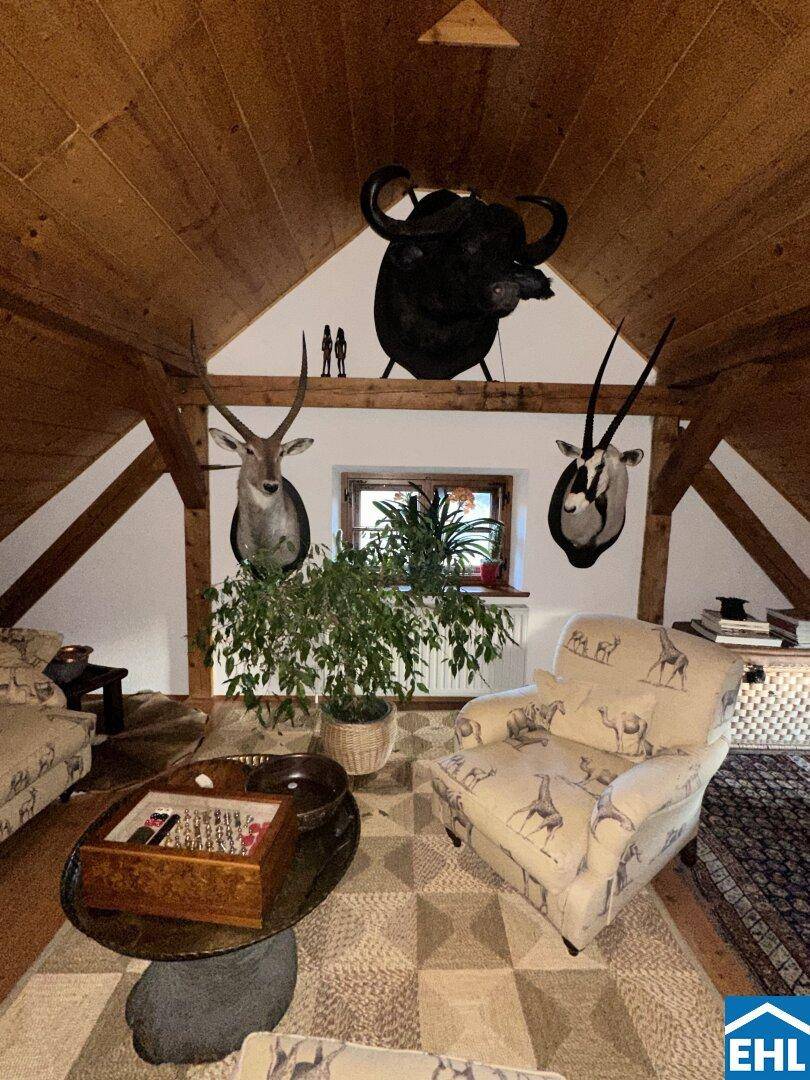 Rustikaler Wohnbereich im Dachgeschoss mit Holzwänden, Dachschräge und Jagdtrophäen.