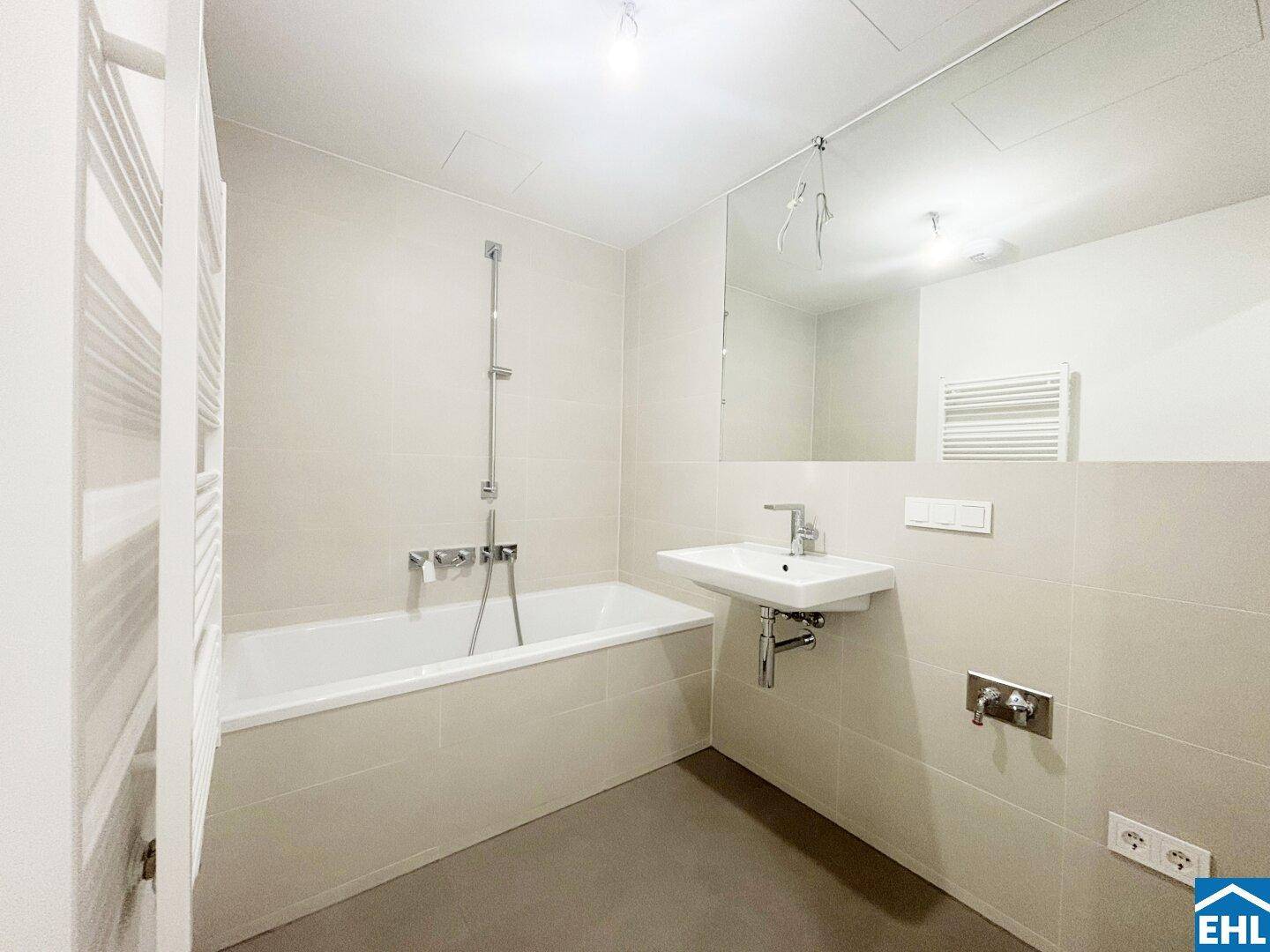 Modernes Badezimmer mit Badewanne, Waschbecken und beheiztem Handtuchhalter in hellen Fliesen.