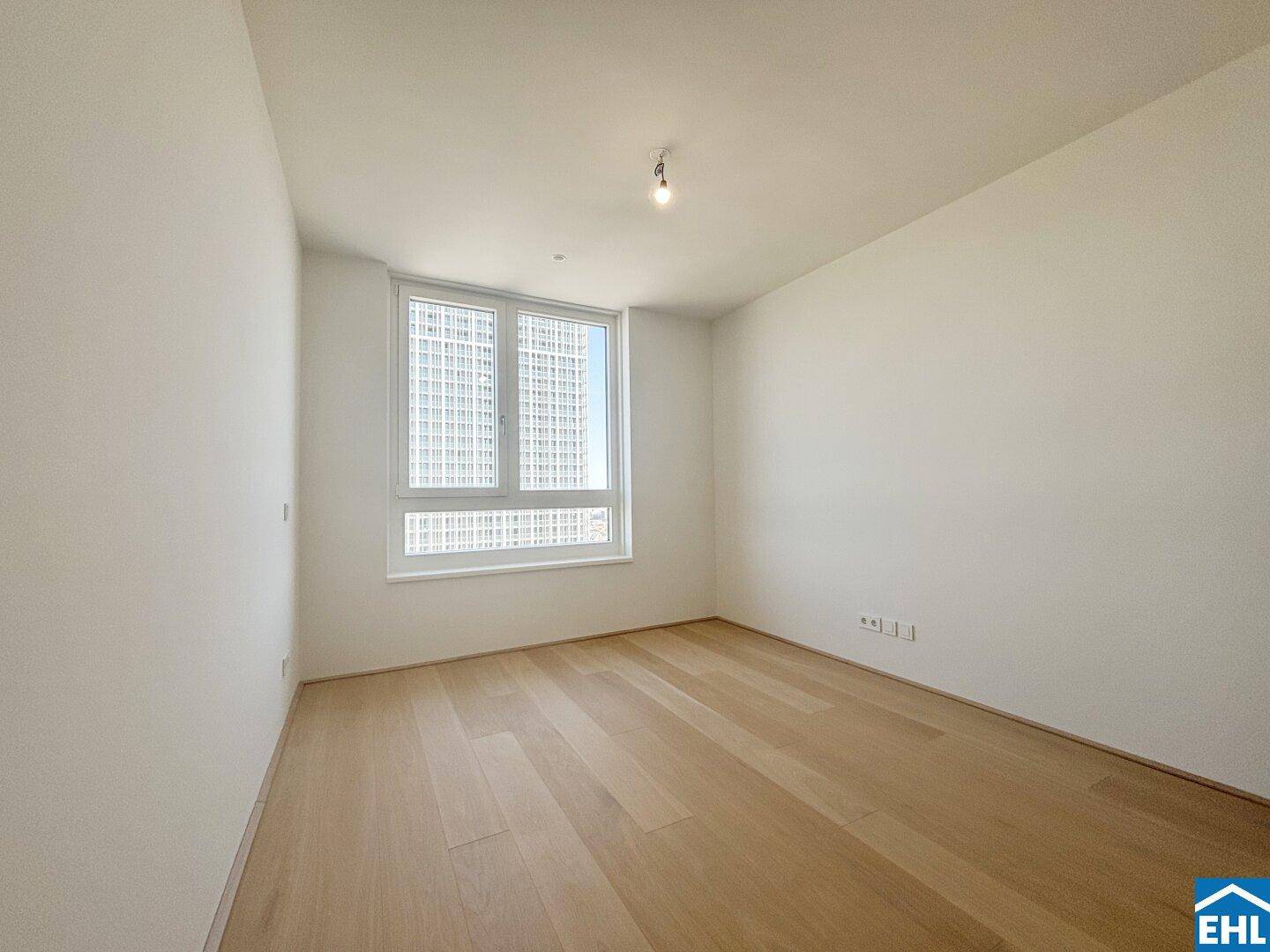 Helles Schlafzimmer mit Holzboden und großem Fenster, das viel Tageslicht hereinlässt.