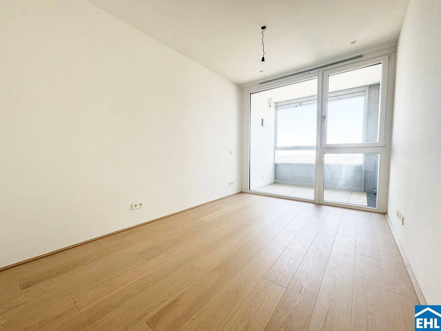 Modernes Zimmer mit hellem Parkettboden und raumhohen Fenstern, die Zugang zu einem Balkon bieten.