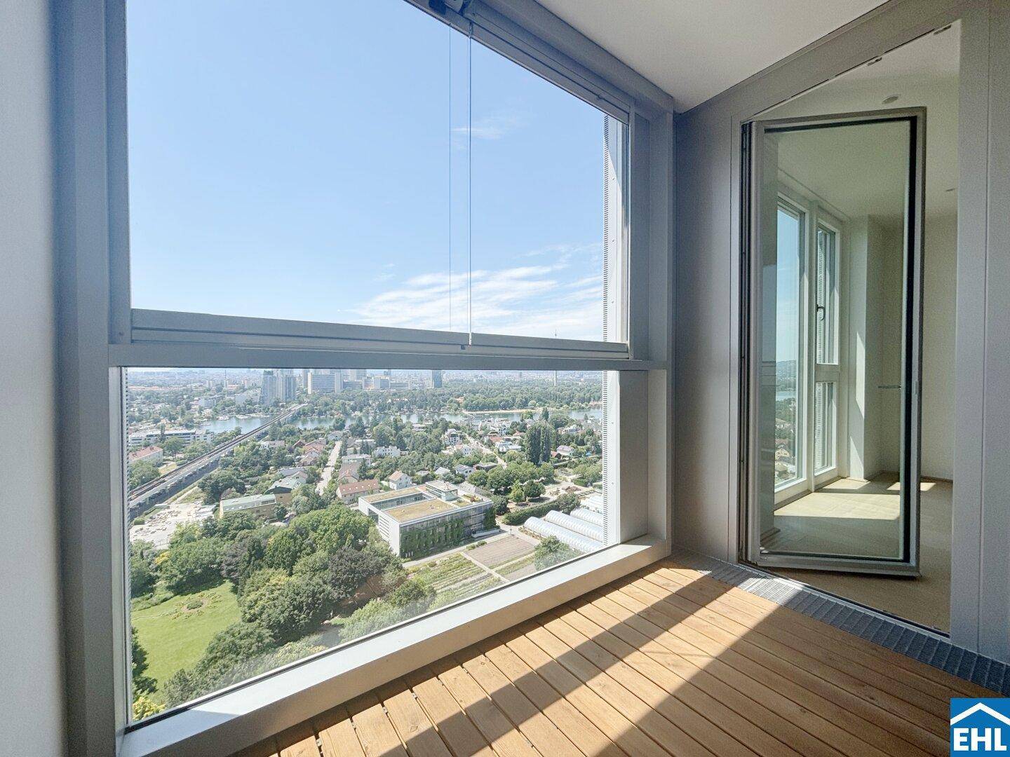 Verglaster Balkon mit Holzboden und weitem Blick über die Stadt und umliegende Grünflächen.