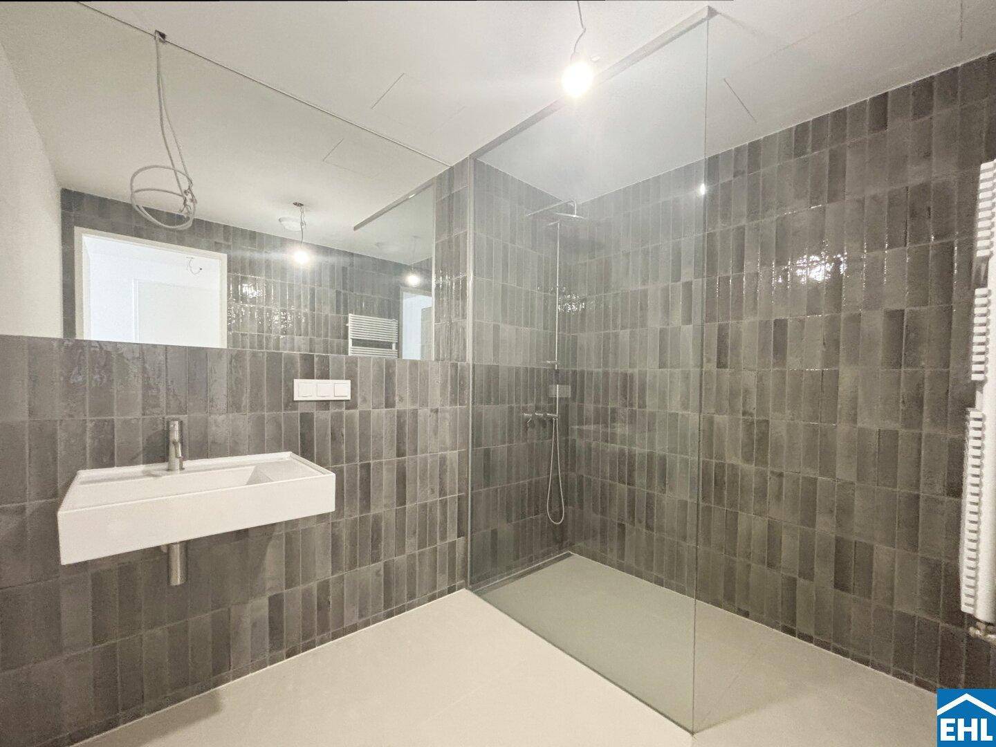 Modernes Badezimmer mit grauen Fliesen, einer großen begehbaren Dusche und einem Wandwaschbecken.