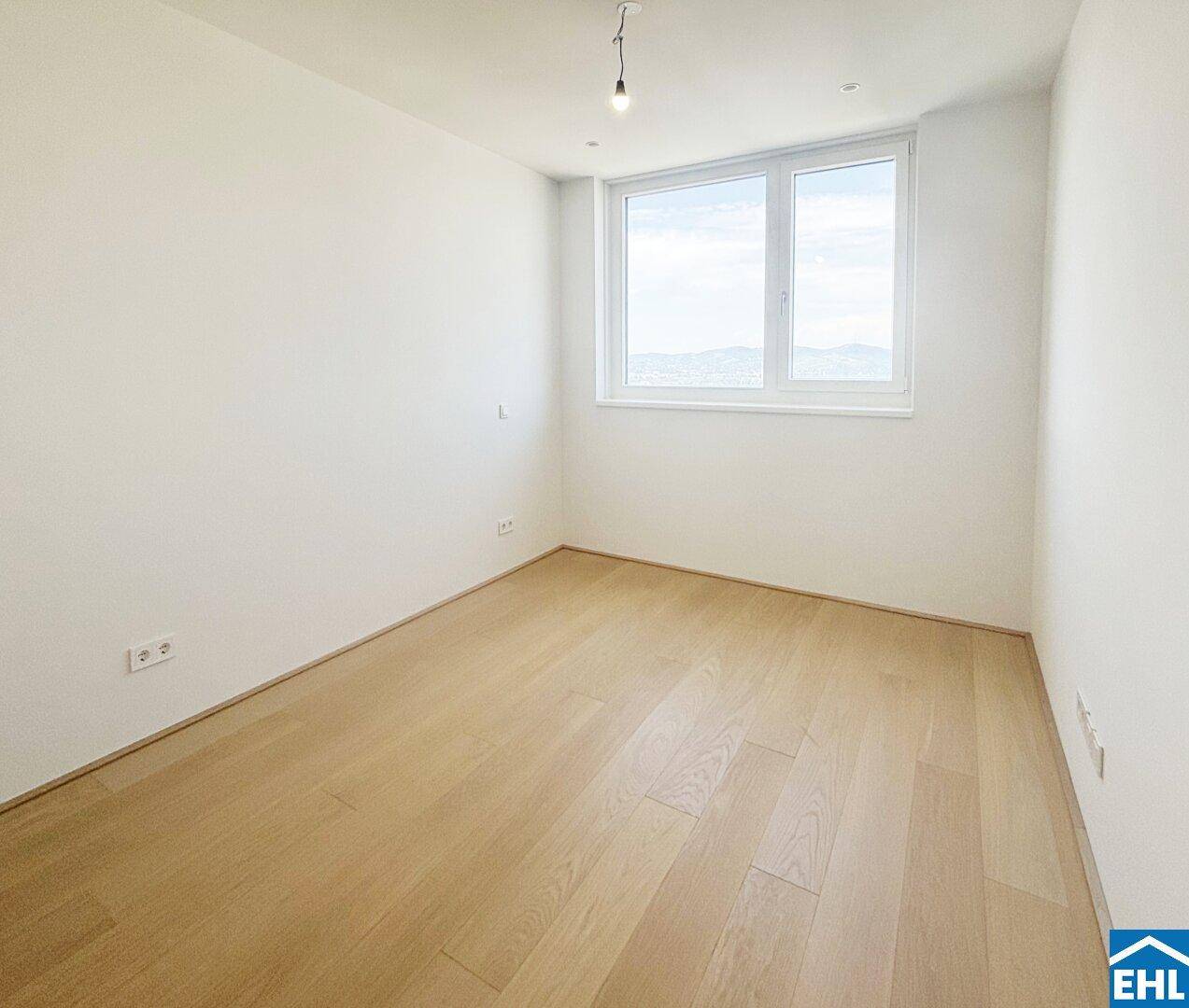 Unmöbliertes Zimmer mit hellem Holzboden und einem großen Fenster für viel Tageslicht.