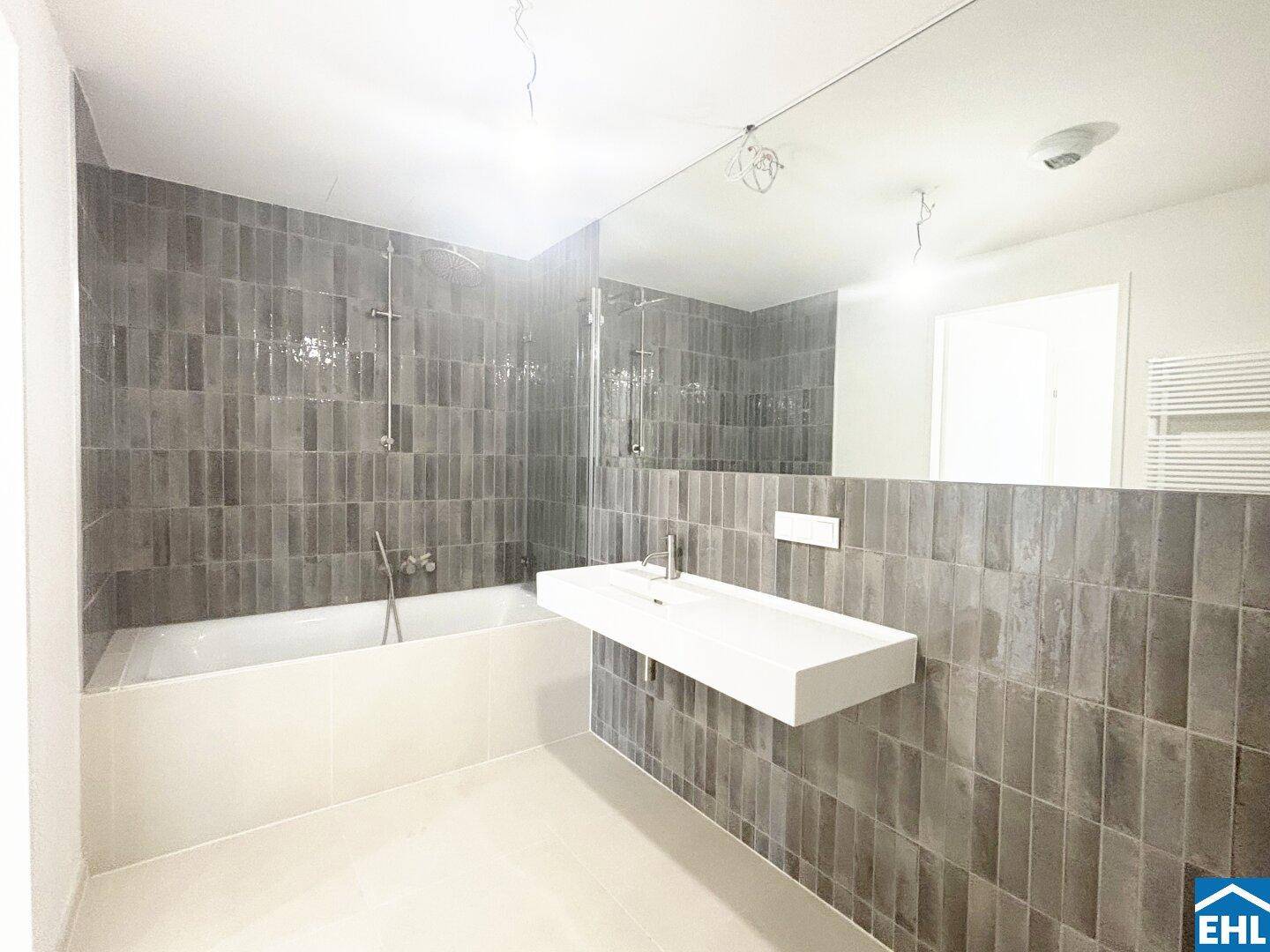 Modernes Badezimmer mit grauen Fliesen, Badewanne und schwebendem Waschbecken.
