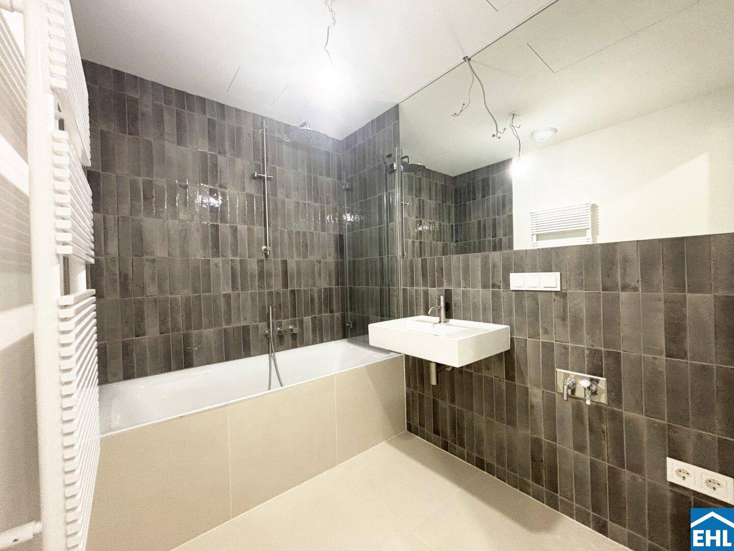 Modernes Badezimmer mit dunklen Fliesen, Badewanne und einem einzelnen Waschbecken.