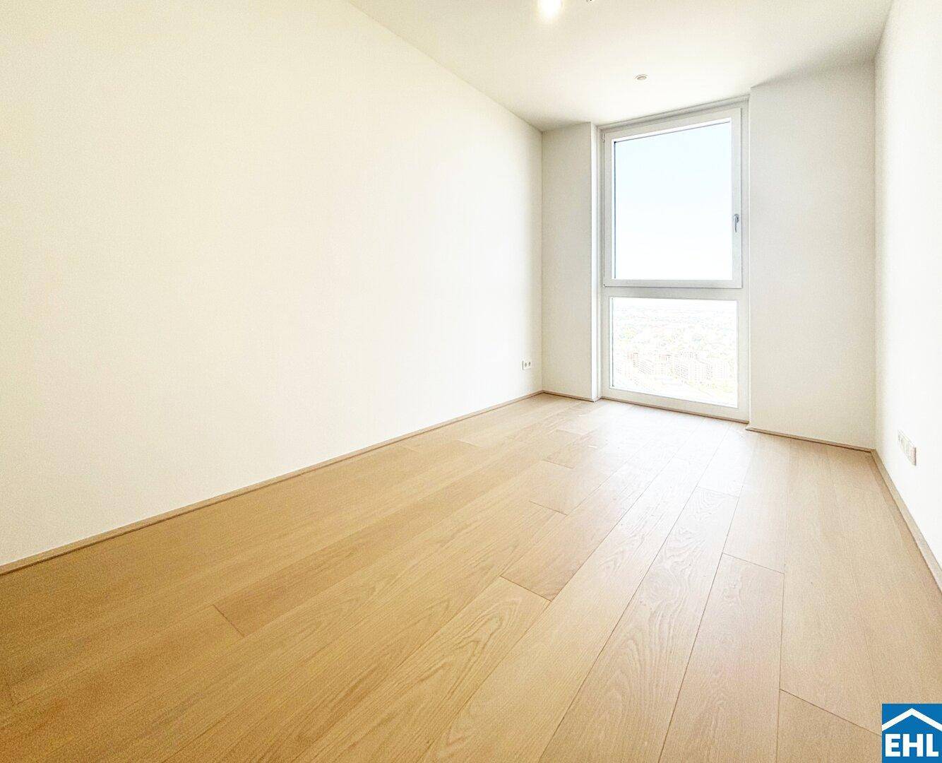 Helles Zimmer mit Holzboden und einem großen Fenster, ideal als Schlaf- oder Arbeitszimmer.