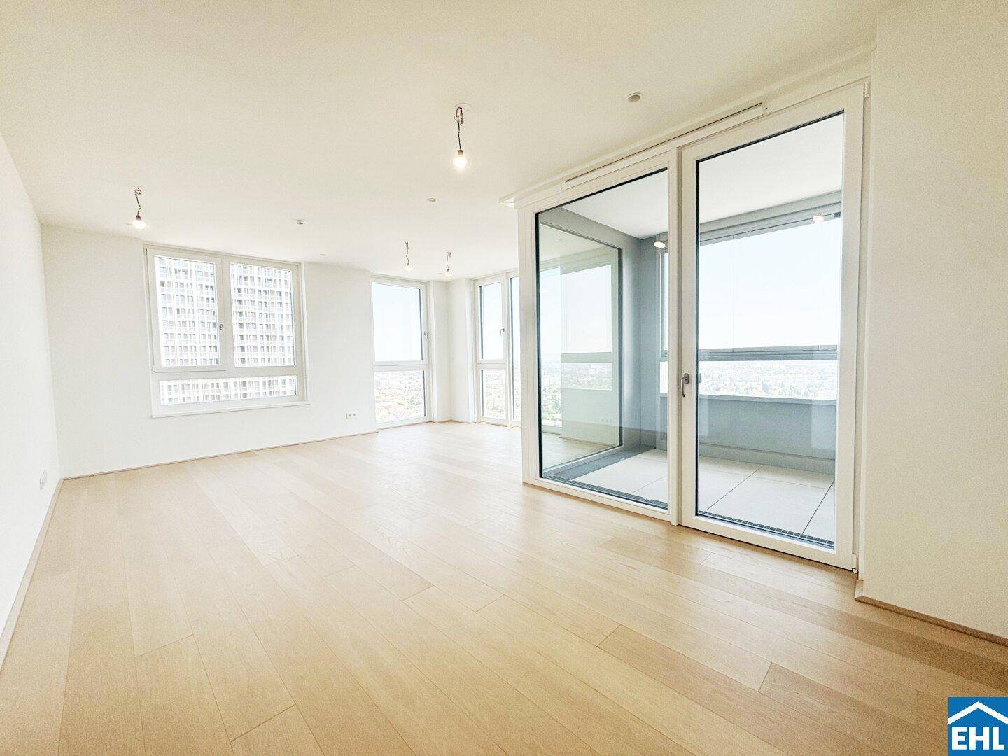 Geräumiges, helles Zimmer mit Holzboden und Zugang zu einem verglasten Balkon mit Weitblick.