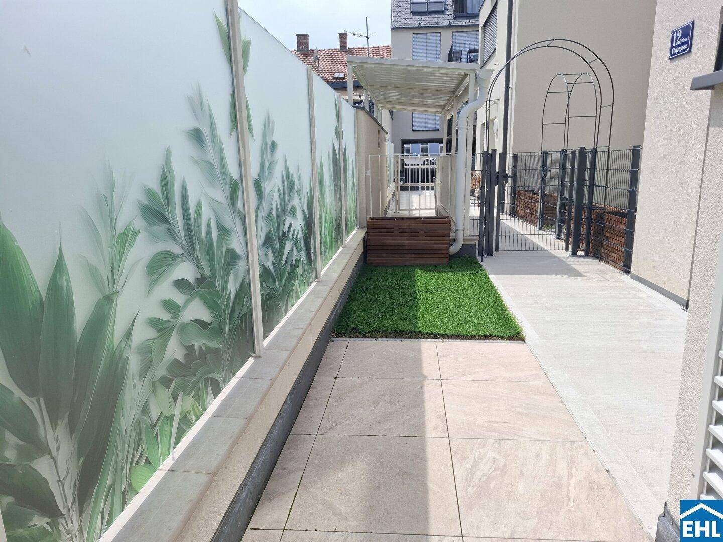 Außenbereich mit gepflasterter Terrasse, Kunstrasen und dekorativer Sichtschutzwand.
