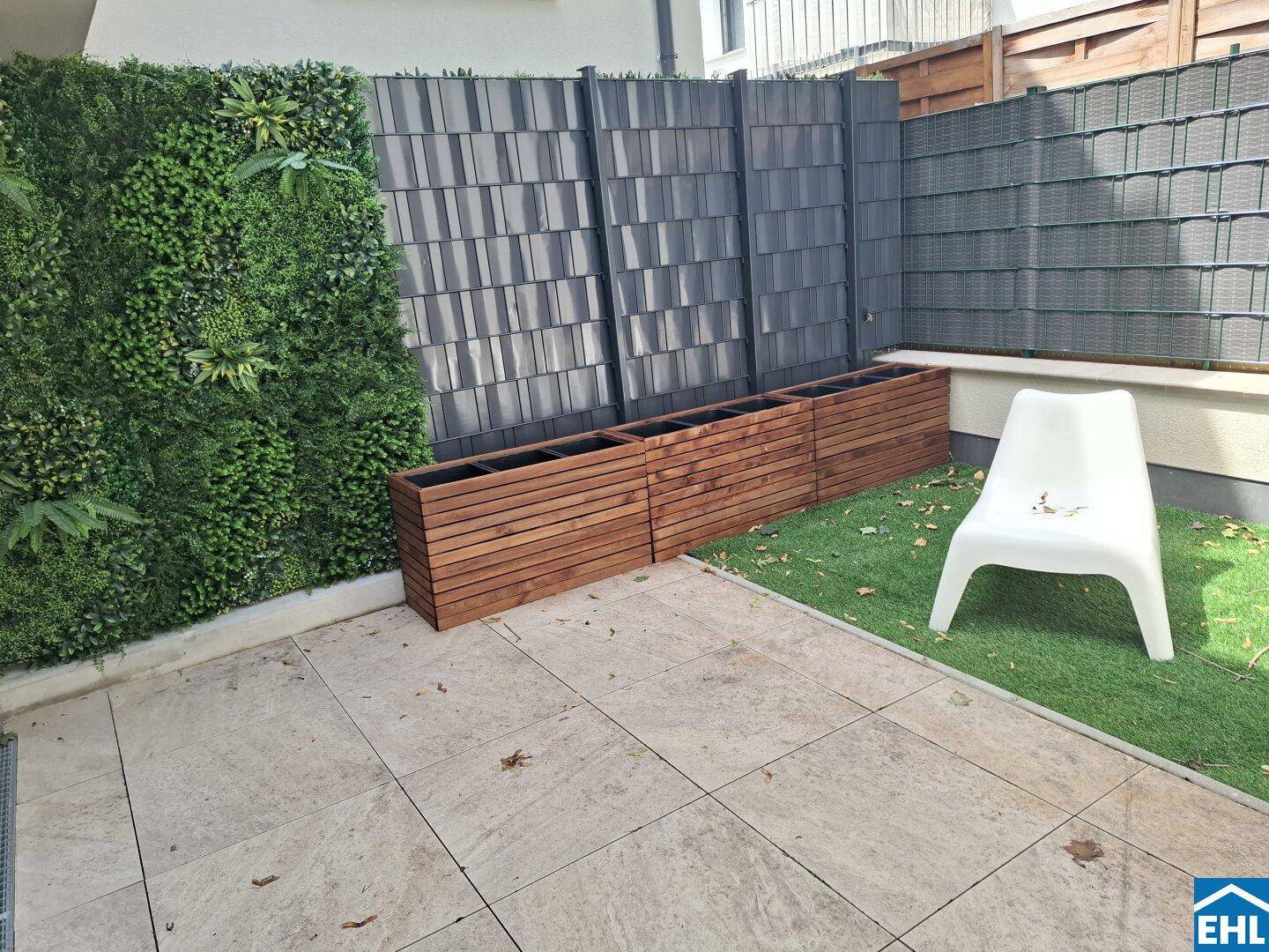 Kleine Terrasse mit Kunstrasen, Pflanzkübeln und vertikaler Begrünung als Sichtschutz.