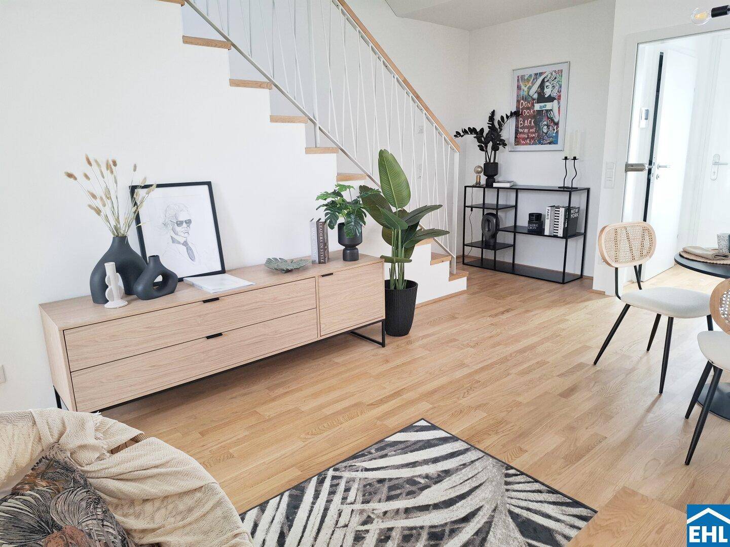 Geräumiger Wohnbereich mit Holzboden, moderner Einrichtung und offener Treppe zum Obergeschoss.