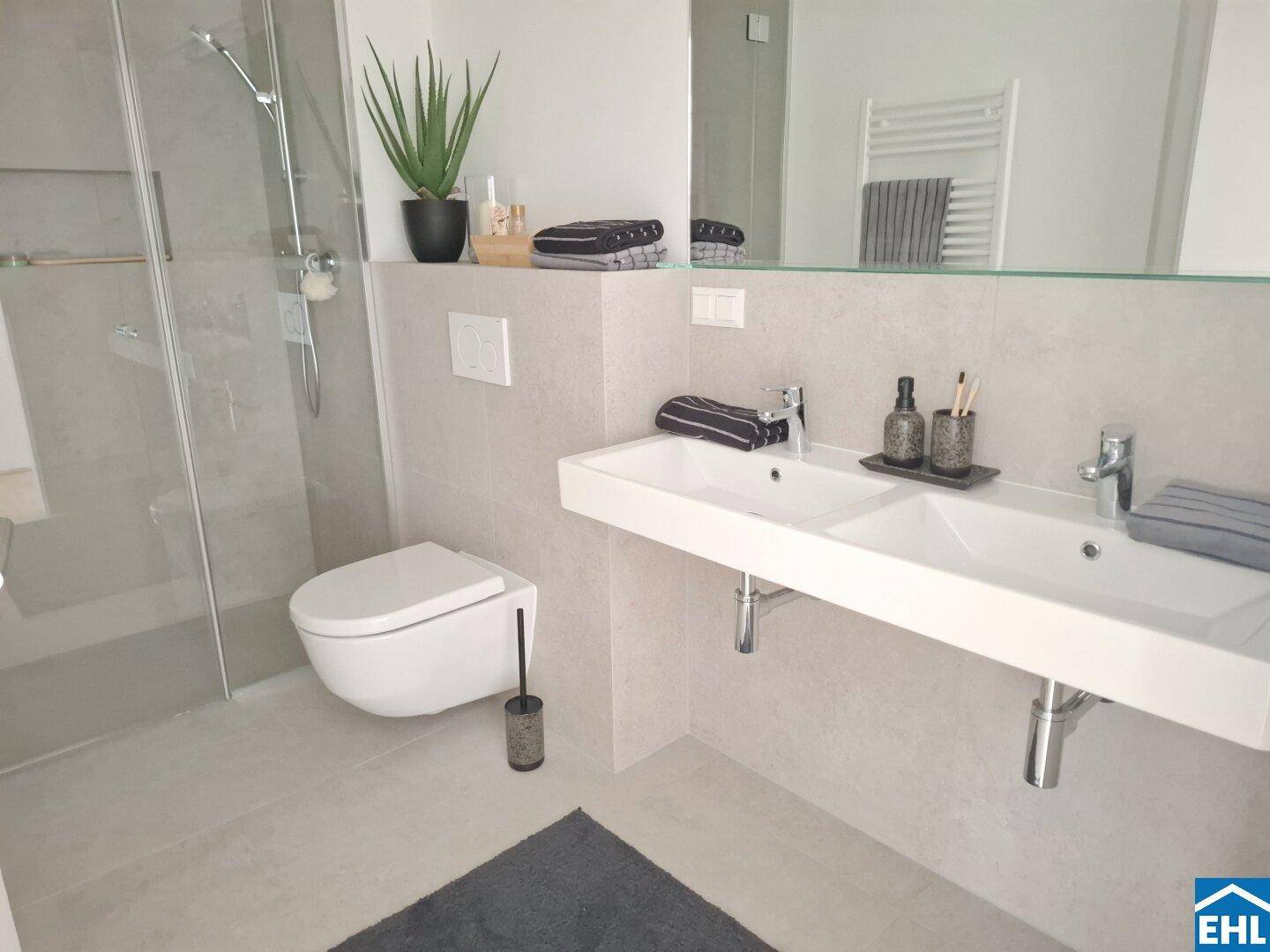 Modernes Badezimmer mit Doppelwaschbecken, wandhängendem WC und ebenerdiger Dusche.
