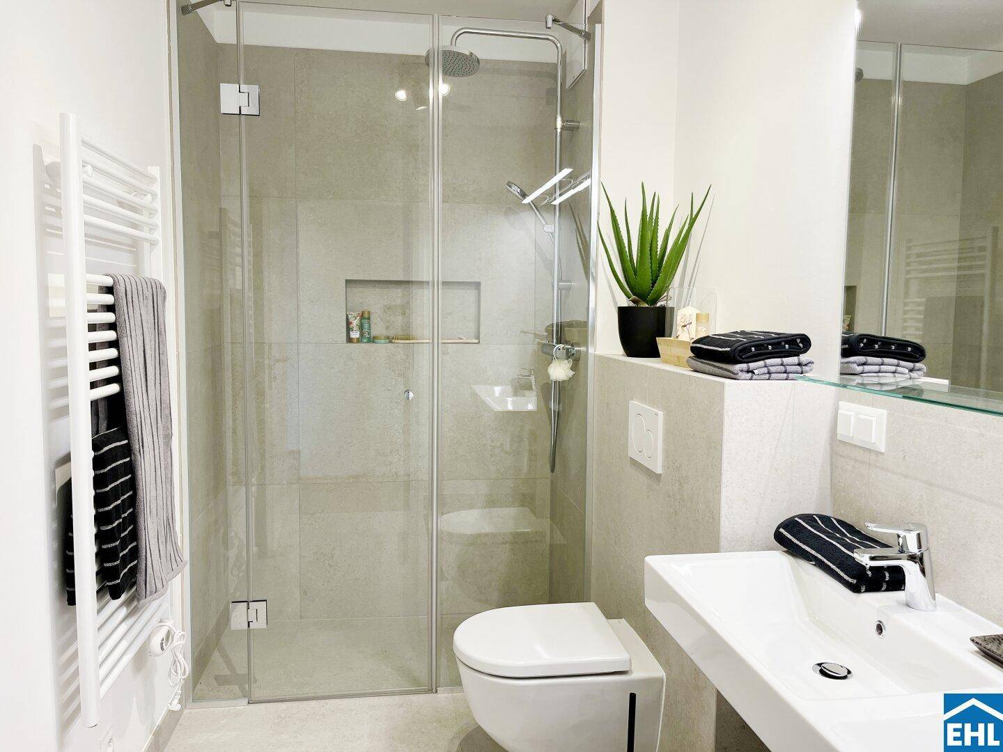 Elegantes Badezimmer mit großer Glasdusche, Wand-WC und beheiztem Handtuchhalter.