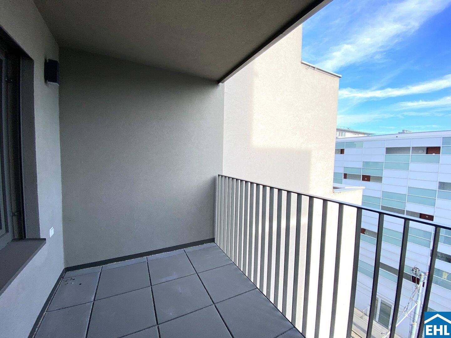 Kleiner Balkon mit Fliesenboden und Metallgeländer, bietet Blick auf umliegende Gebäude.