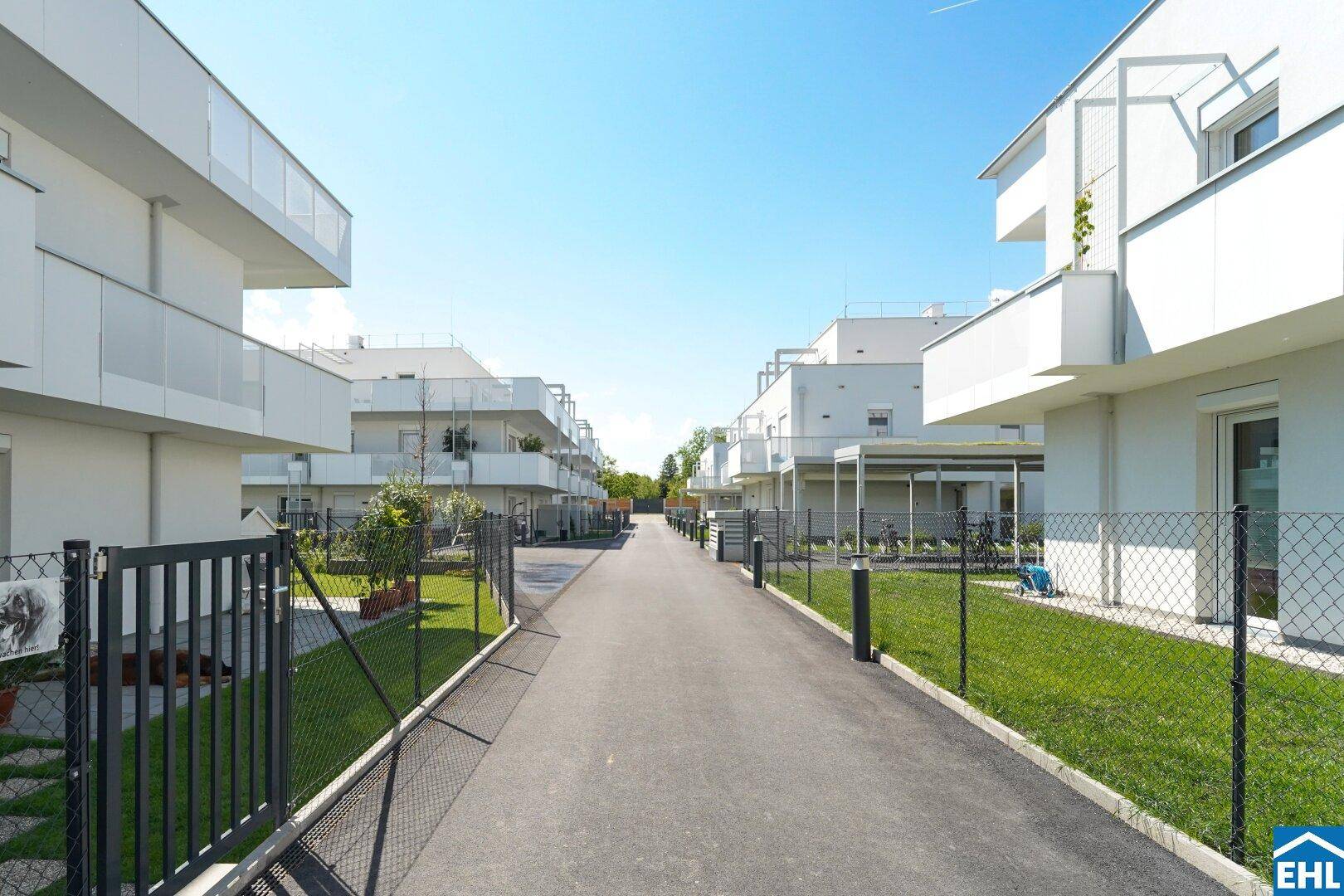 Weitläufige Ansicht einer modernen Wohnsiedlung mit weißen Gebäuden, Grünflächen und einem zentralen Weg.