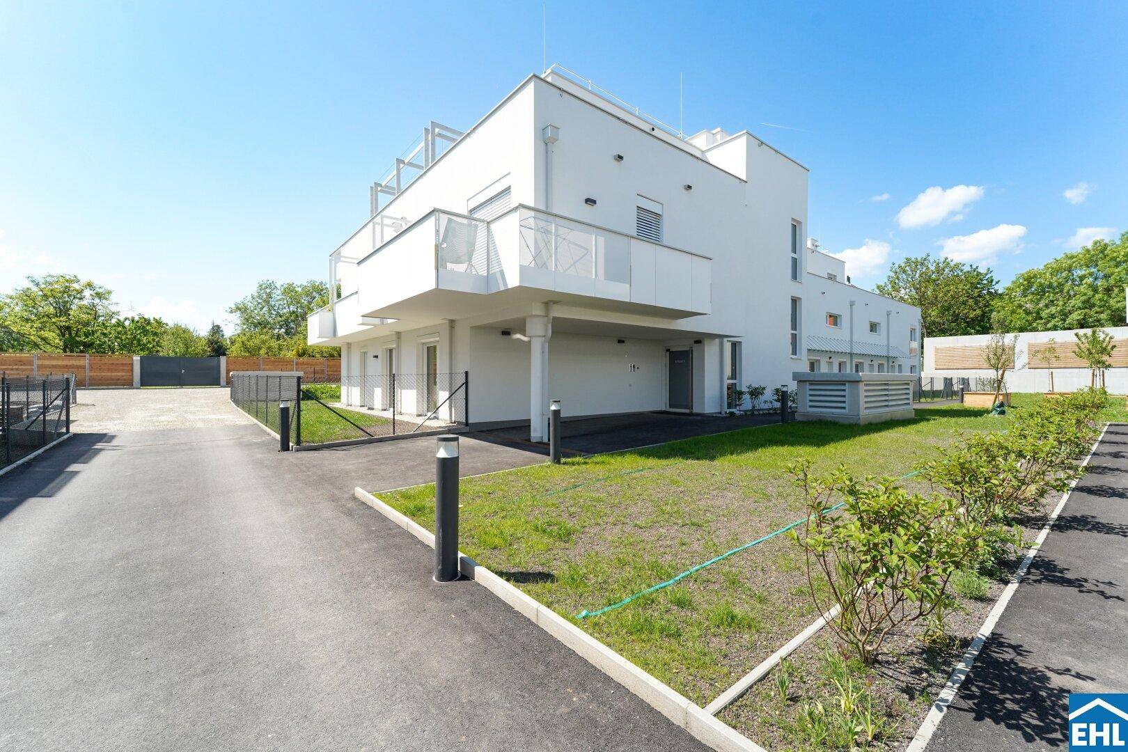Außenansicht eines modernen Wohngebäudes mit weißer Fassade, Balkonen und einer gepflegten Rasenfläche.