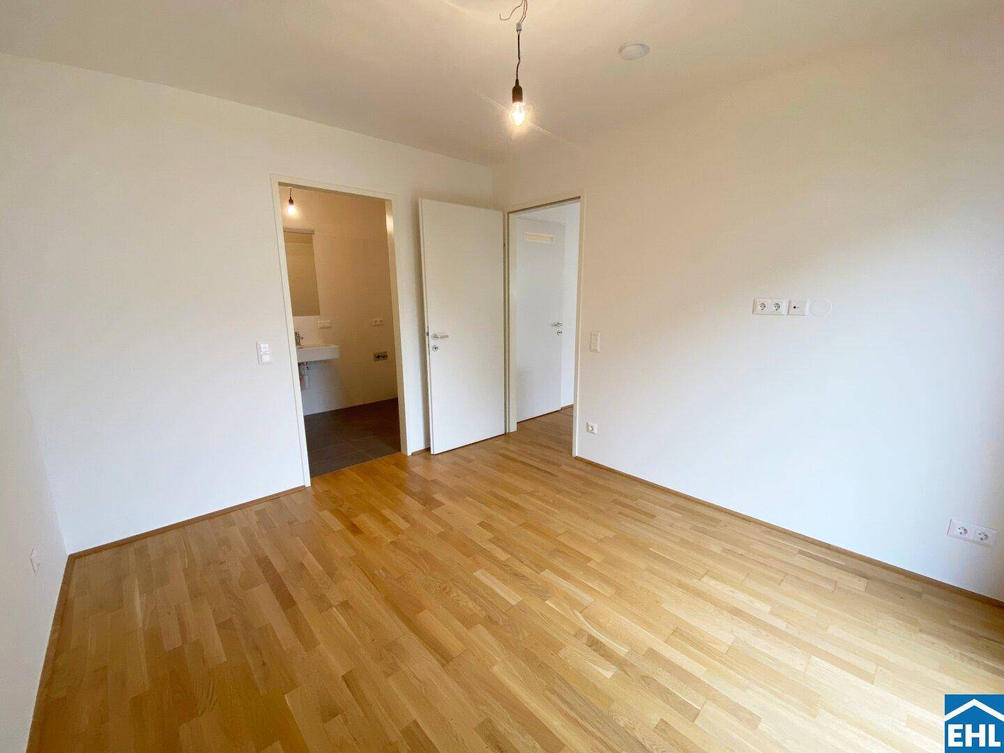 Leerer Raum mit Parkettboden und weißen Wänden, angrenzend an weitere Zimmer.