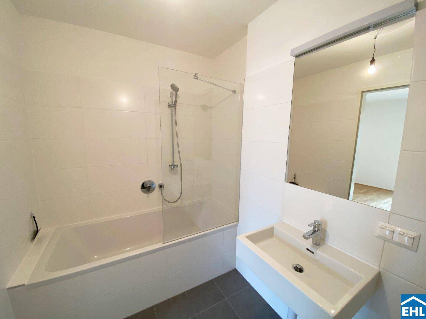 Modernes Badezimmer mit Badewanne, Duschfunktion, Waschbecken und weißen Fliesen.