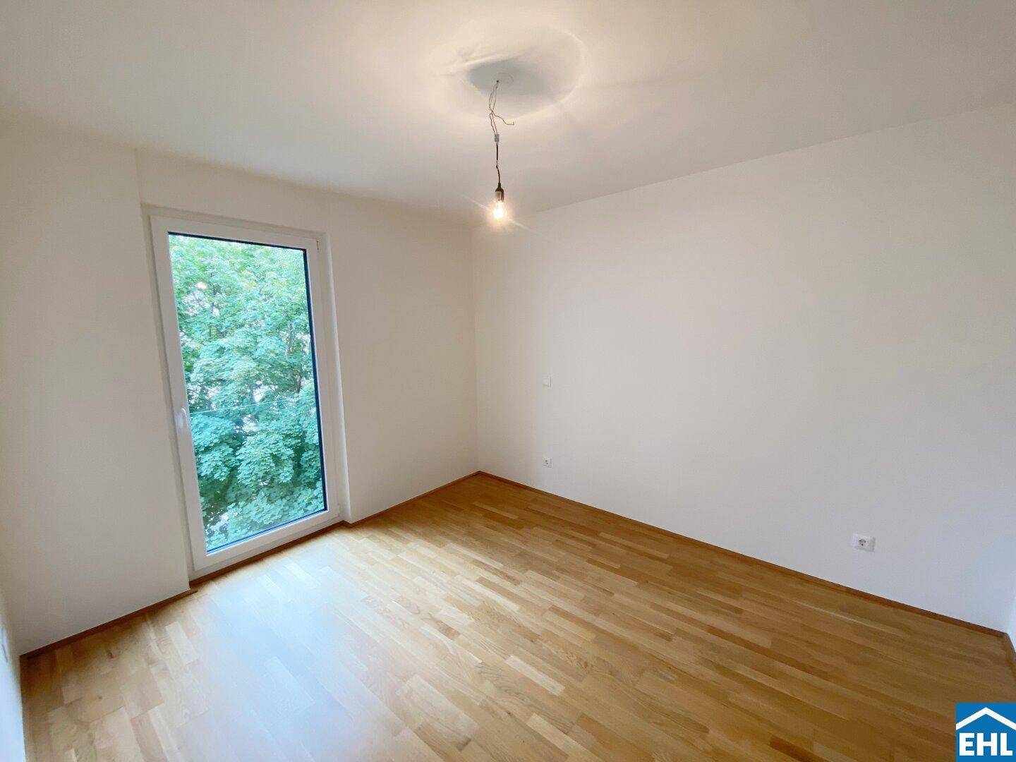Helles Schlafzimmer mit Parkettboden, großen Fenstern und Blick ins Grüne.