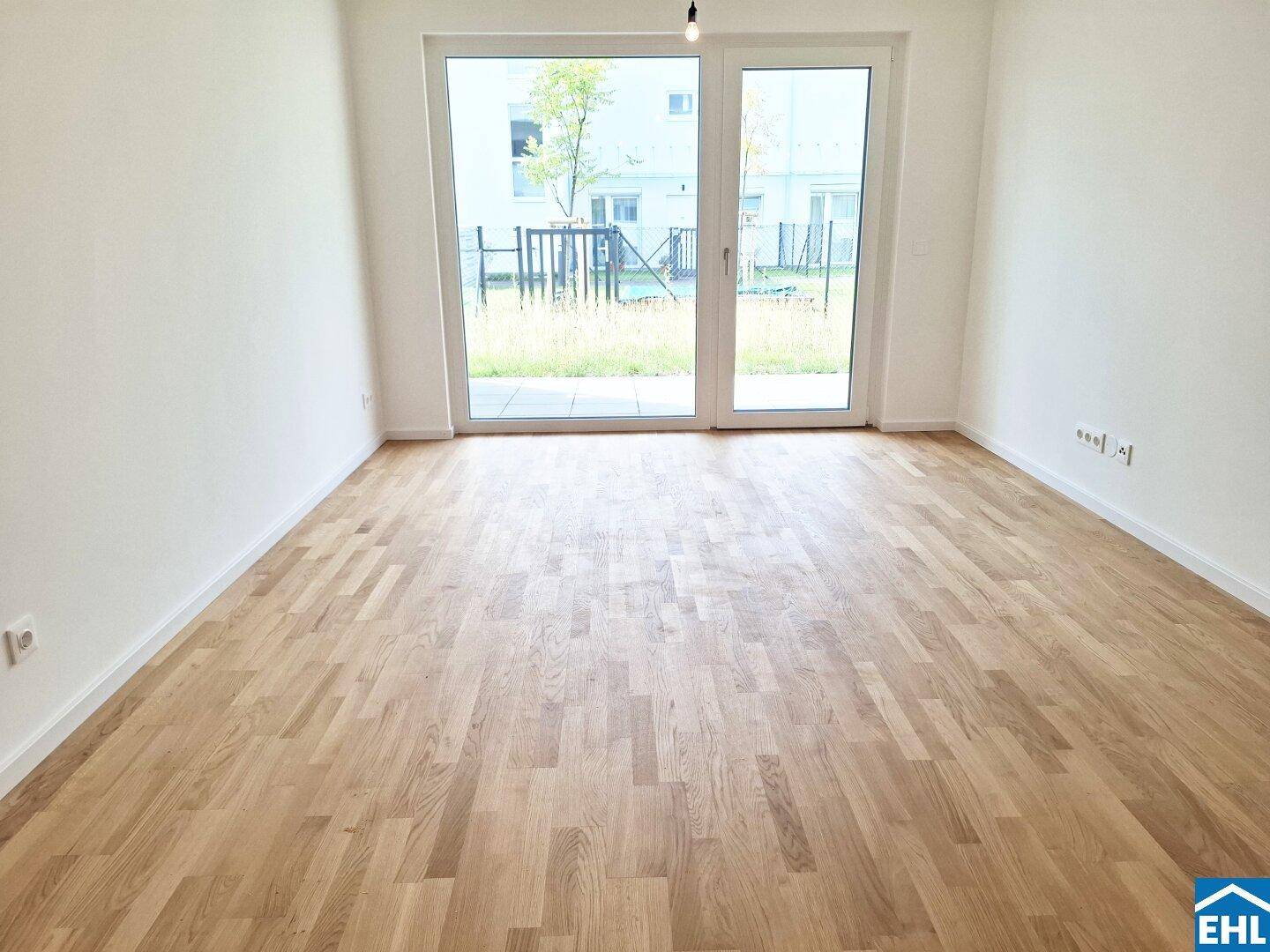 Geräumiger, leerer Raum mit Holzboden und großen Fenstertüren zum Außenbereich.