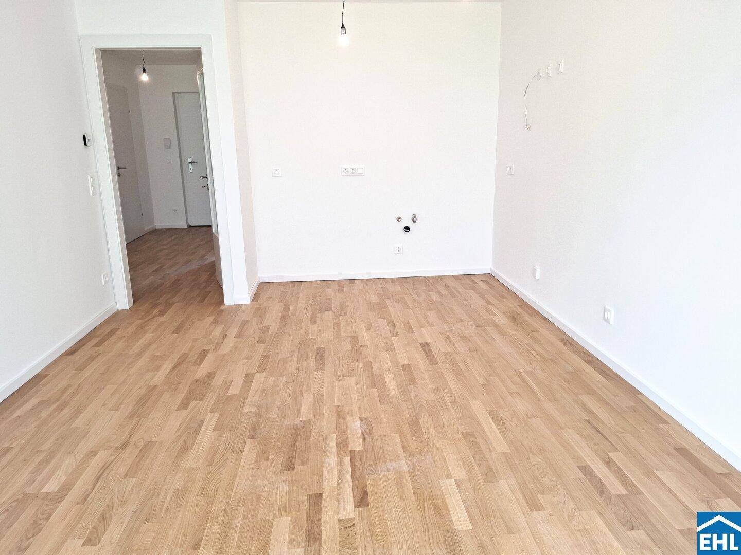 Leerer Raum, vorbereitet für eine moderne Küche, mit Holzboden und weißen Wänden.