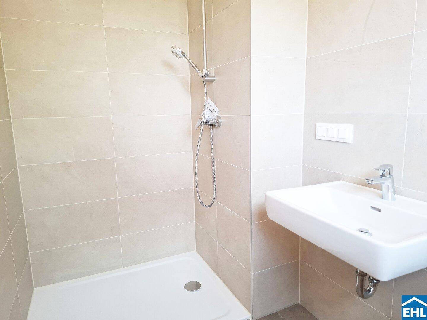 Funktionales Badezimmer mit Duschbereich, Einzelwaschbecken und hellen Wandfliesen.