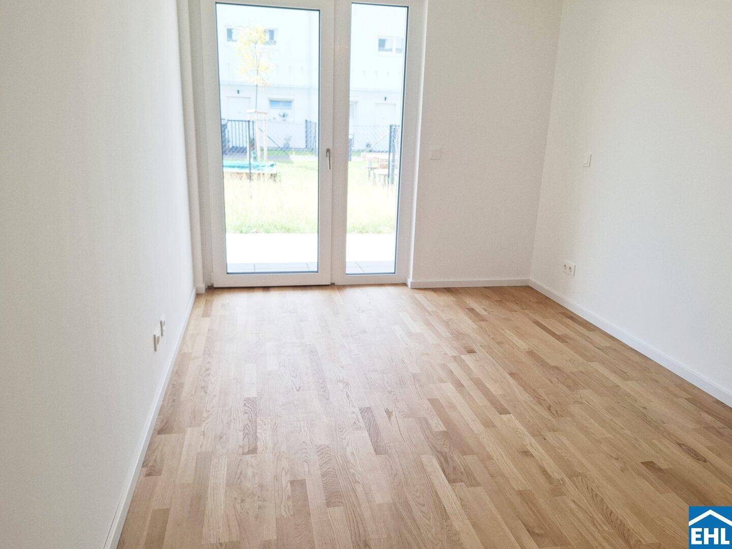 Heller, unmöblierter Raum mit Holzboden und Zugang zu einem kleinen Gartenbereich.
