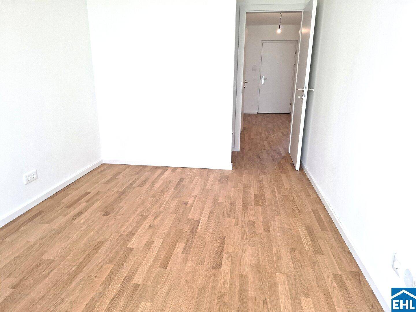 Heller, leerer Raum mit Holzboden und Zugang zu einem weiteren Zimmer.