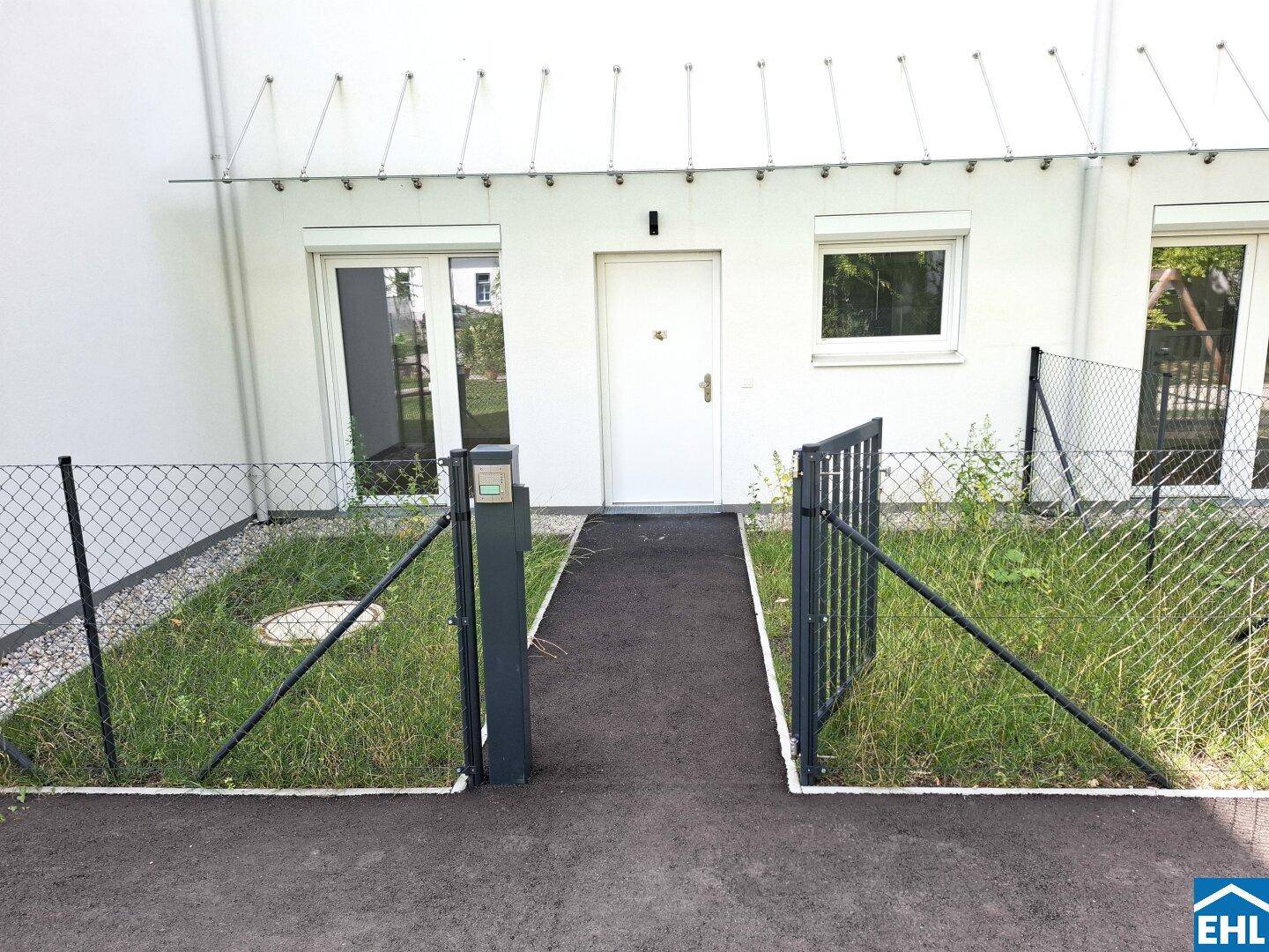 Eingangsbereich eines Hauses mit kleinem, umzäunten Vorgarten und weißer Fassade.