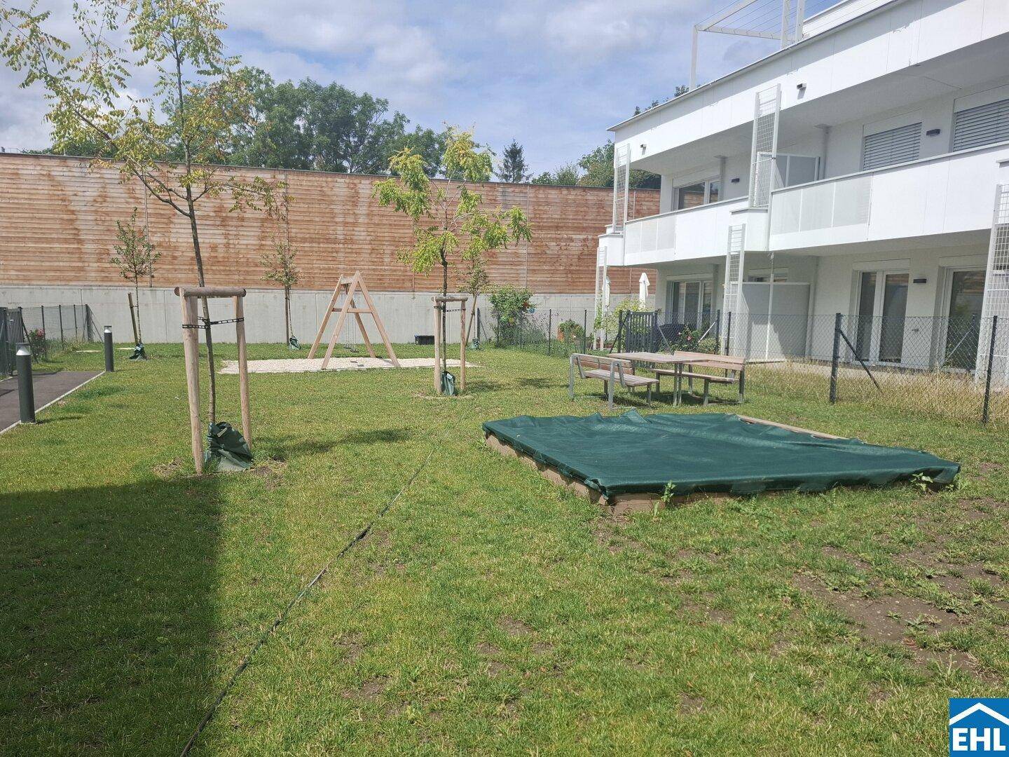 Gepflegte Grünfläche mit Sandkasten, Schaukel und Picknicktisch für Familien in der Wohnanlage.