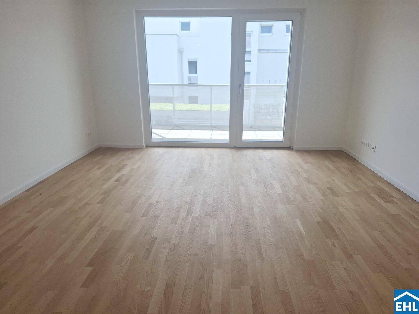Helles Zimmer mit neuem Parkettboden und großem Fenster mit Zugang zum Balkon.