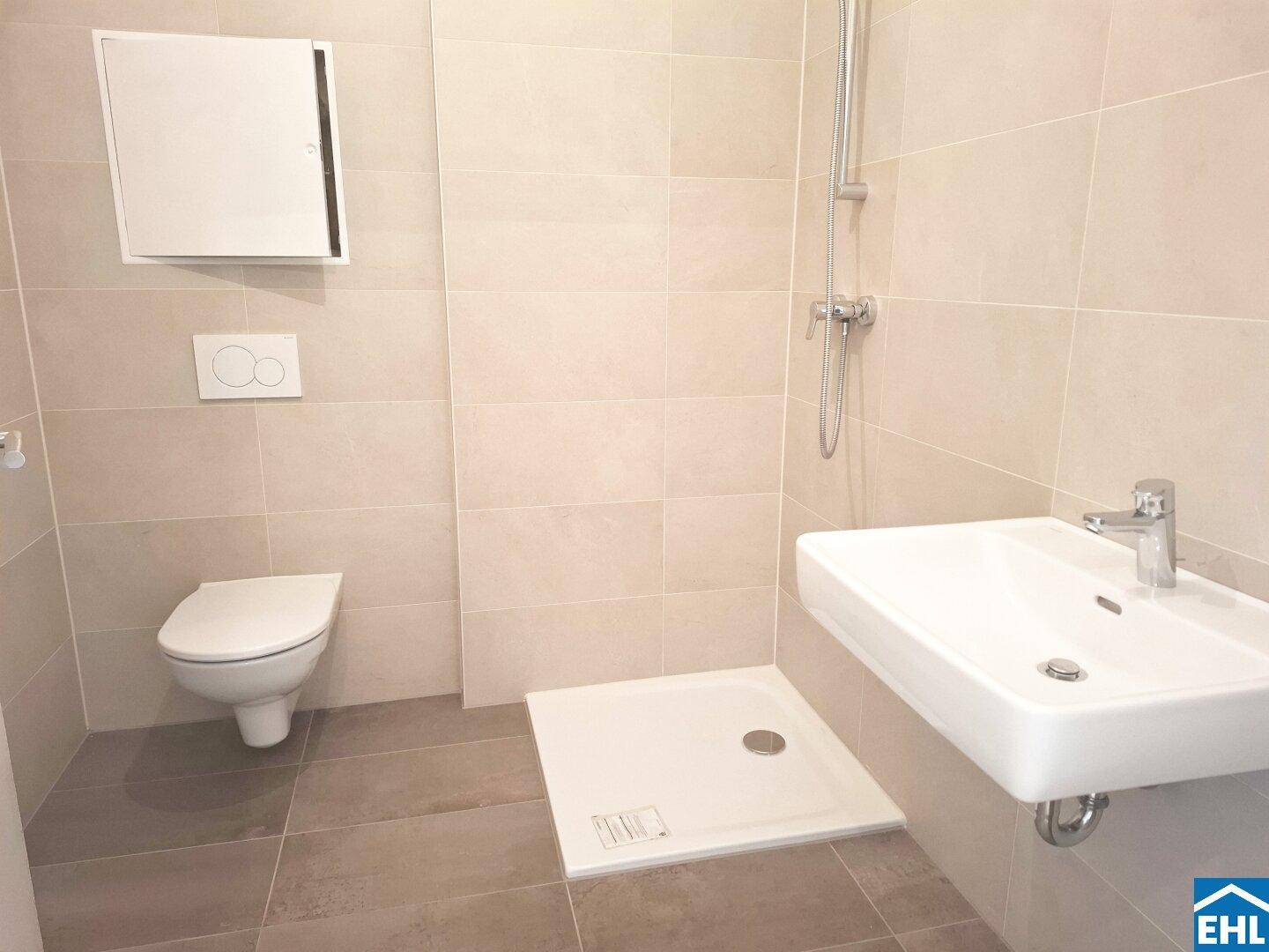 Modernes Badezimmer mit beigefarbenen Fliesen, wandhängendem WC, Waschbecken und ebenerdiger Dusche.