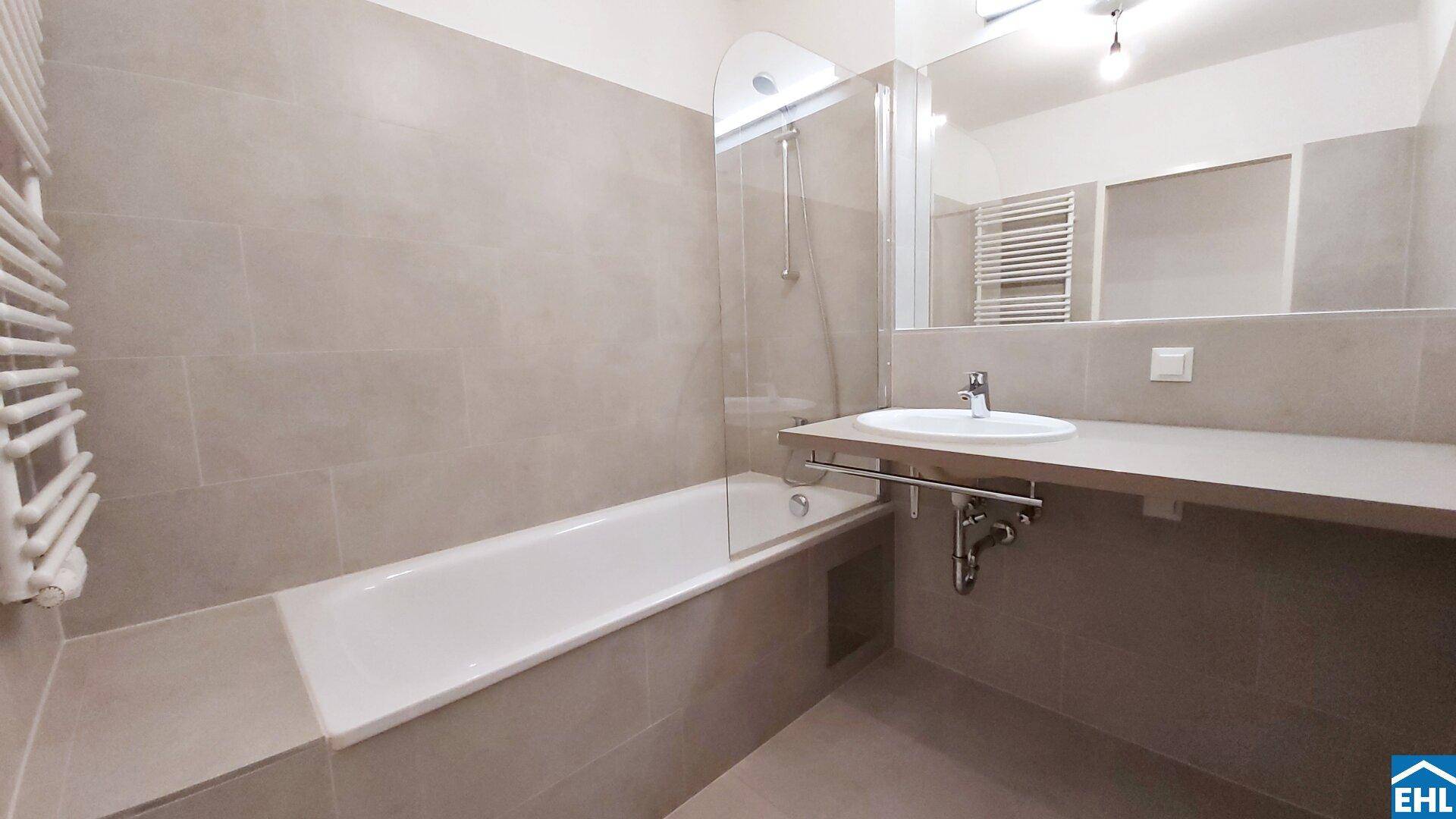 Modernes Badezimmer mit beigefarbenen Fliesen, Badewanne mit Duschabtrennung und Einzelwaschbecken.