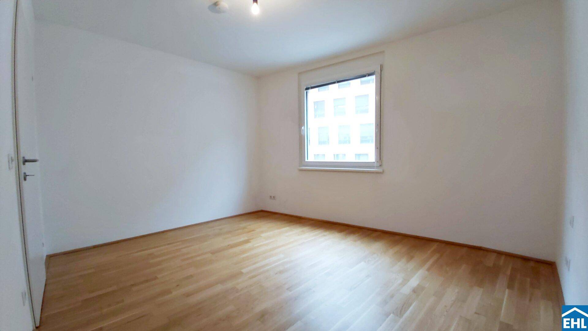 Helles Schlafzimmer mit Parkettboden und einem Fenster, das viel Tageslicht hereinlässt.
