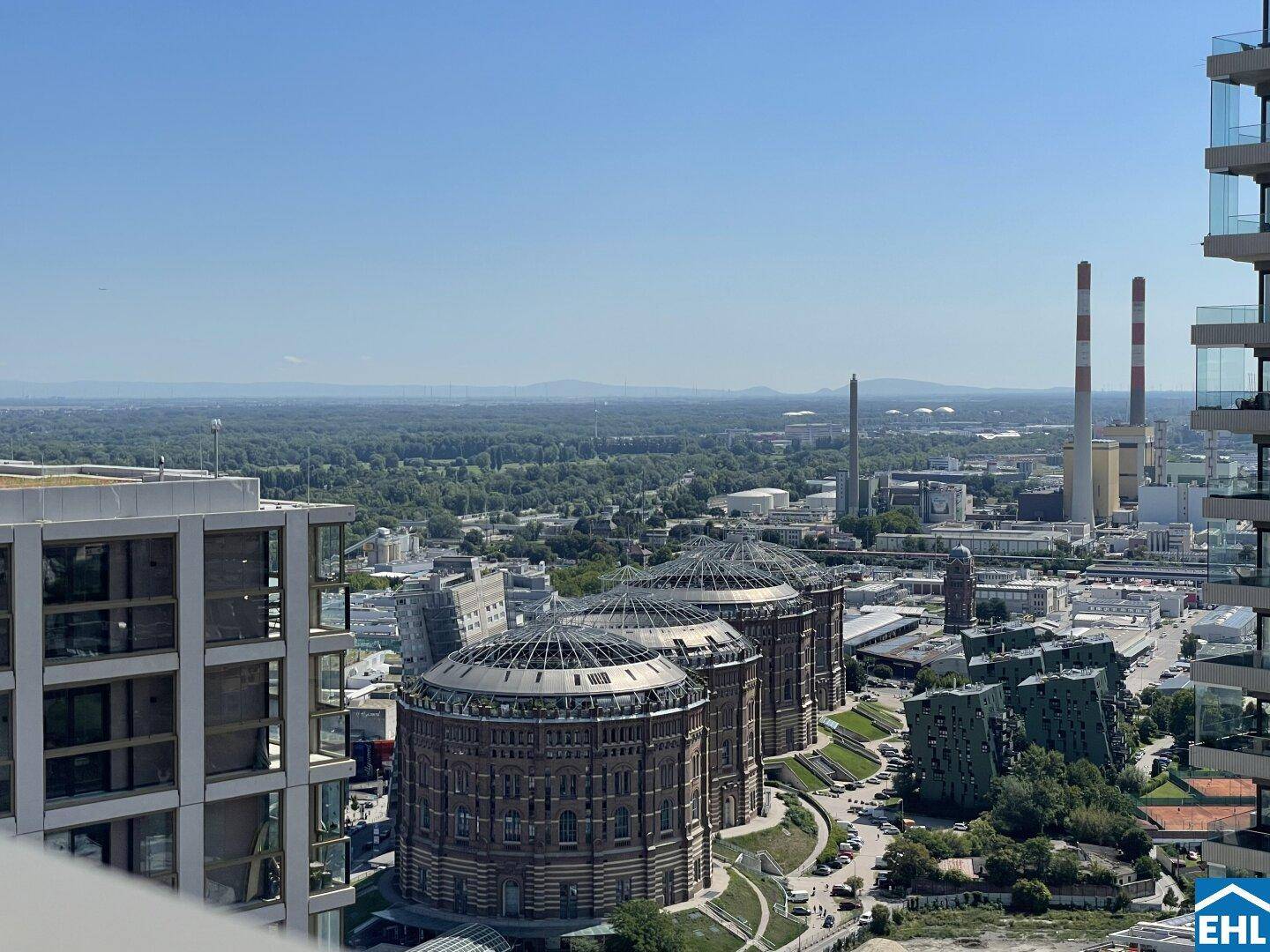Weitläufiger Stadtblick mit historischen Gasometern, Industrieanlagen und grünen Flächen.