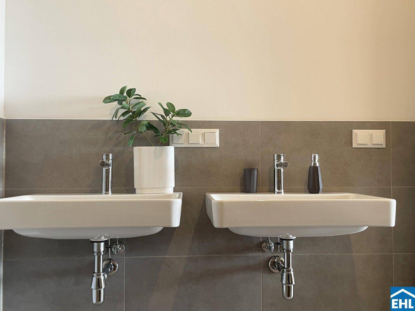 Badezimmer mit zwei Waschbecken und modernen Armaturen auf grauen Fliesen.