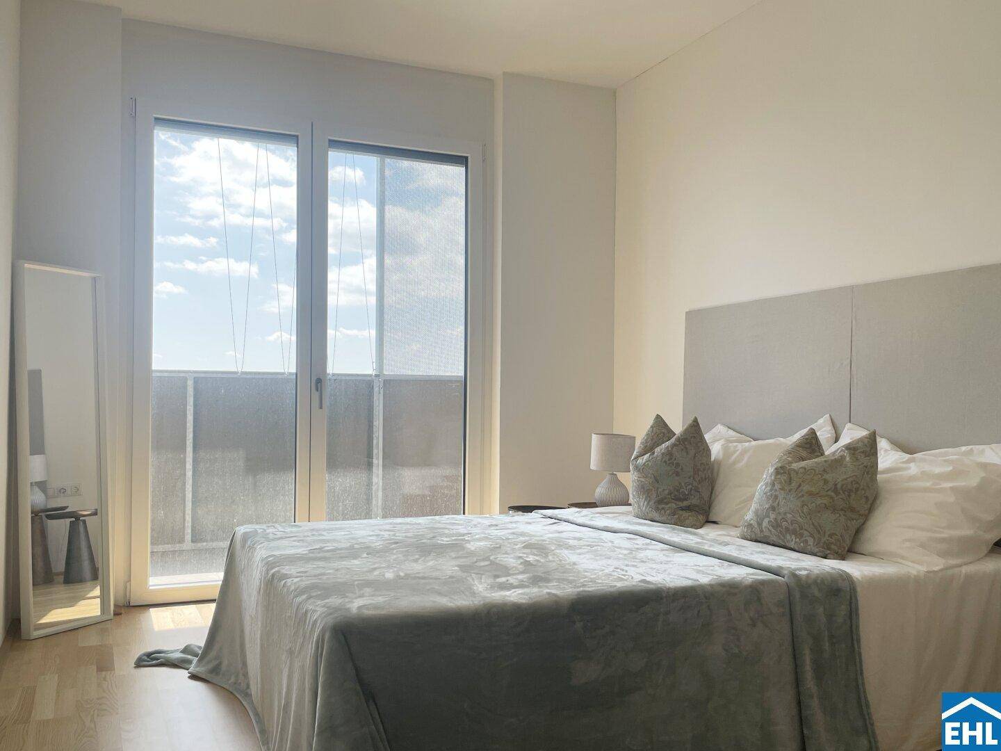 Schlafzimmer mit Doppelbett, hellem Holzboden und Zugang zu einem Balkon.